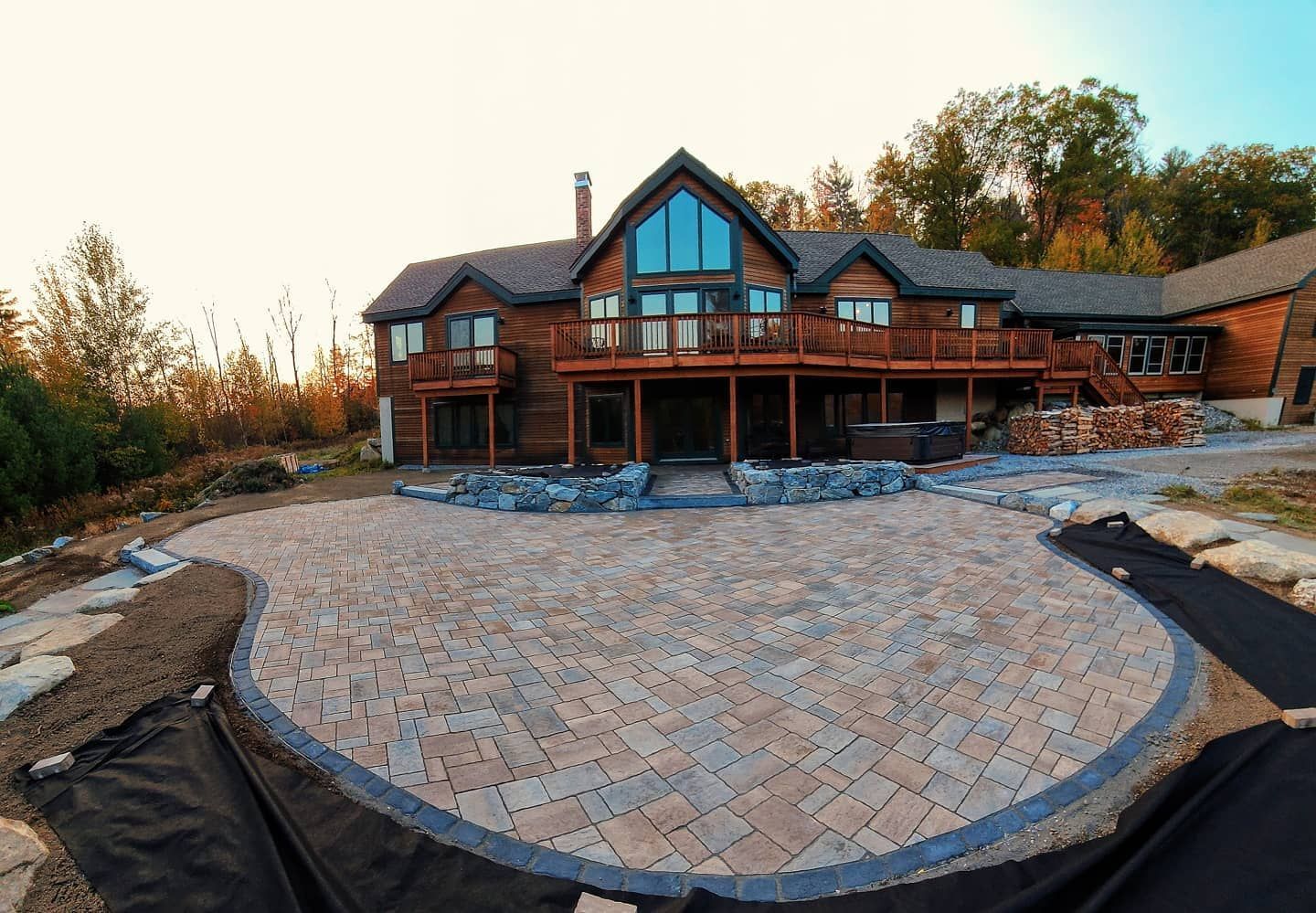 Large wooden house with a spacious, newly installed paver stone patio in the backyard during a sunset.