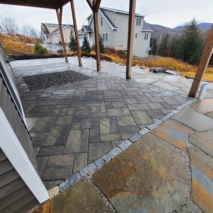 A multi-level patio featuring rectangular gray pavers and large, irregular tan flagstones, framed by a wooden deck structure.