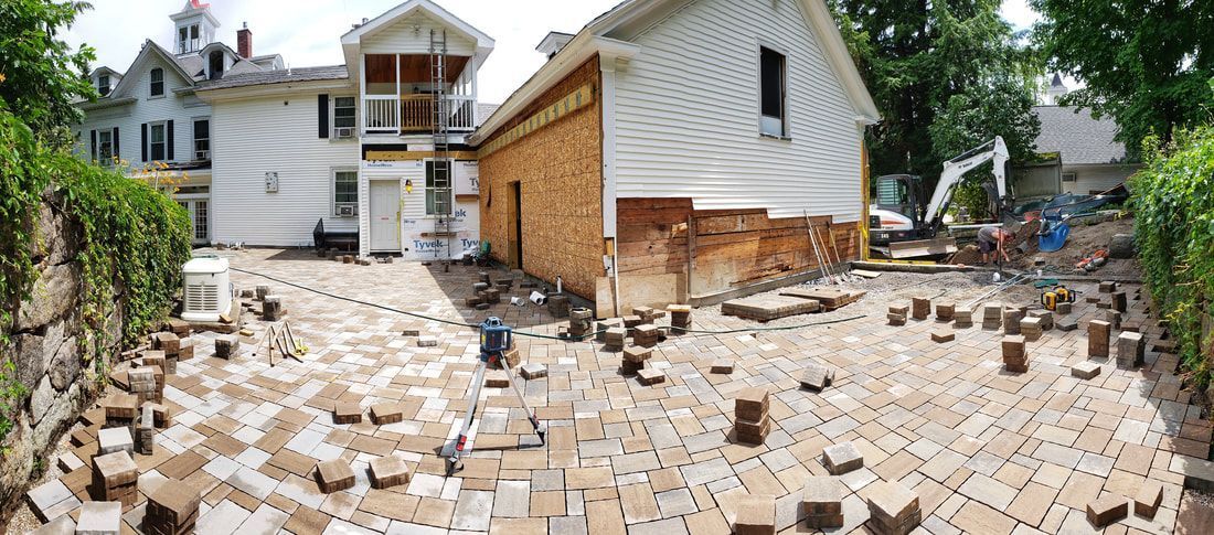 A wide-angle view of a backyard undergoing renovation, with loose paving bricks scattered across the patio area.