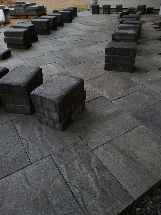 A patio under construction with stacks of rectangular gray pavers arranged on the ground.