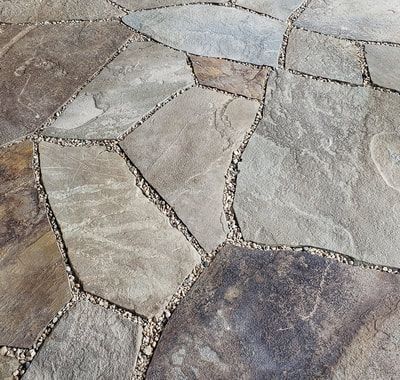 Flagstone patio paving with irregular tan and grey stone slabs separated by small pebbles.