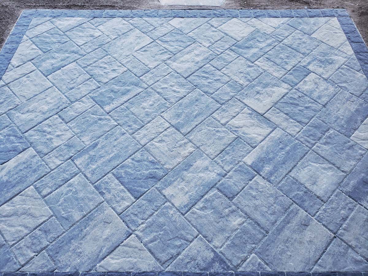 A patio paved with rectangular stone pavers in a geometric, multi-directional pattern featuring shades of blue and gray.