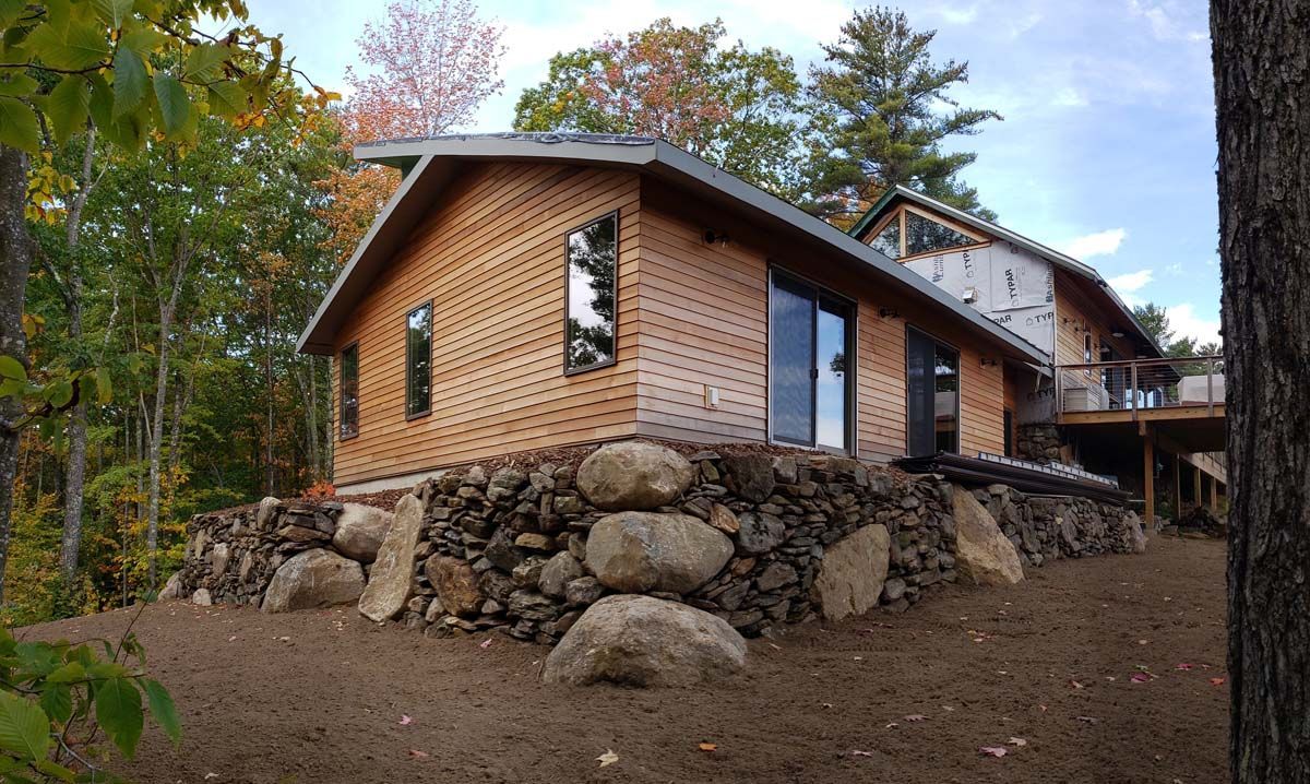 Modern house with wood siding set on a large stone foundation in a forest clearing.