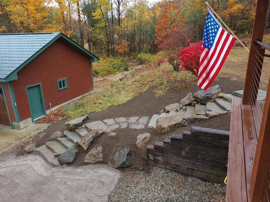 A flag flies over a stone path and stairs leading to a red building near a wooded area in autumn.