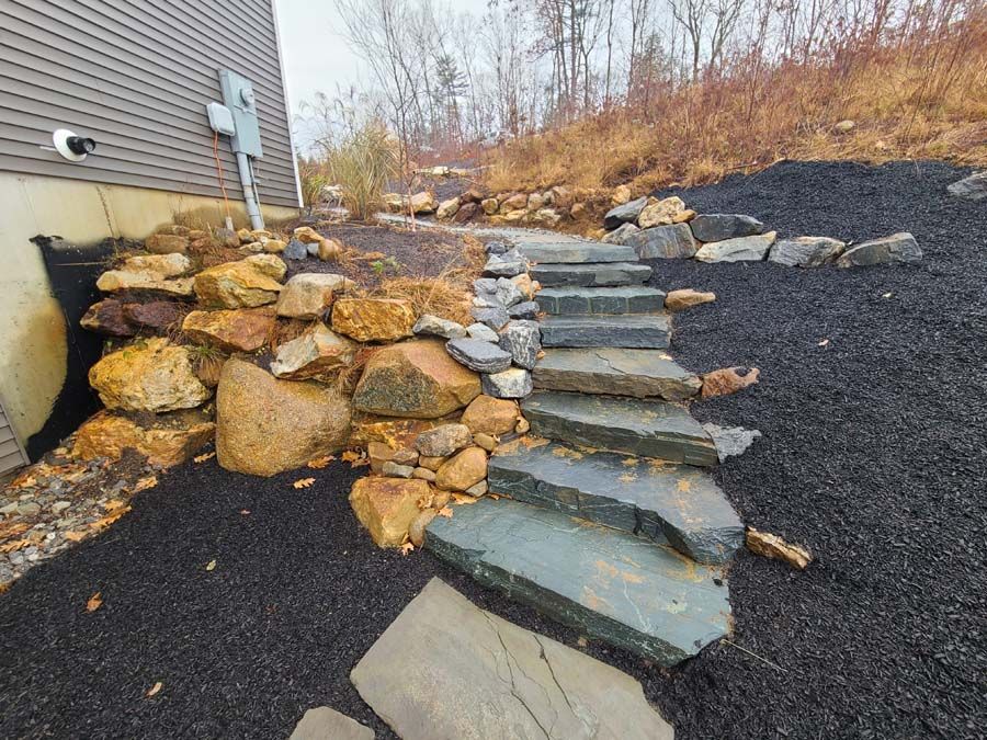 Natural stone steps leading up a slope next to a building with a dark gravel area.