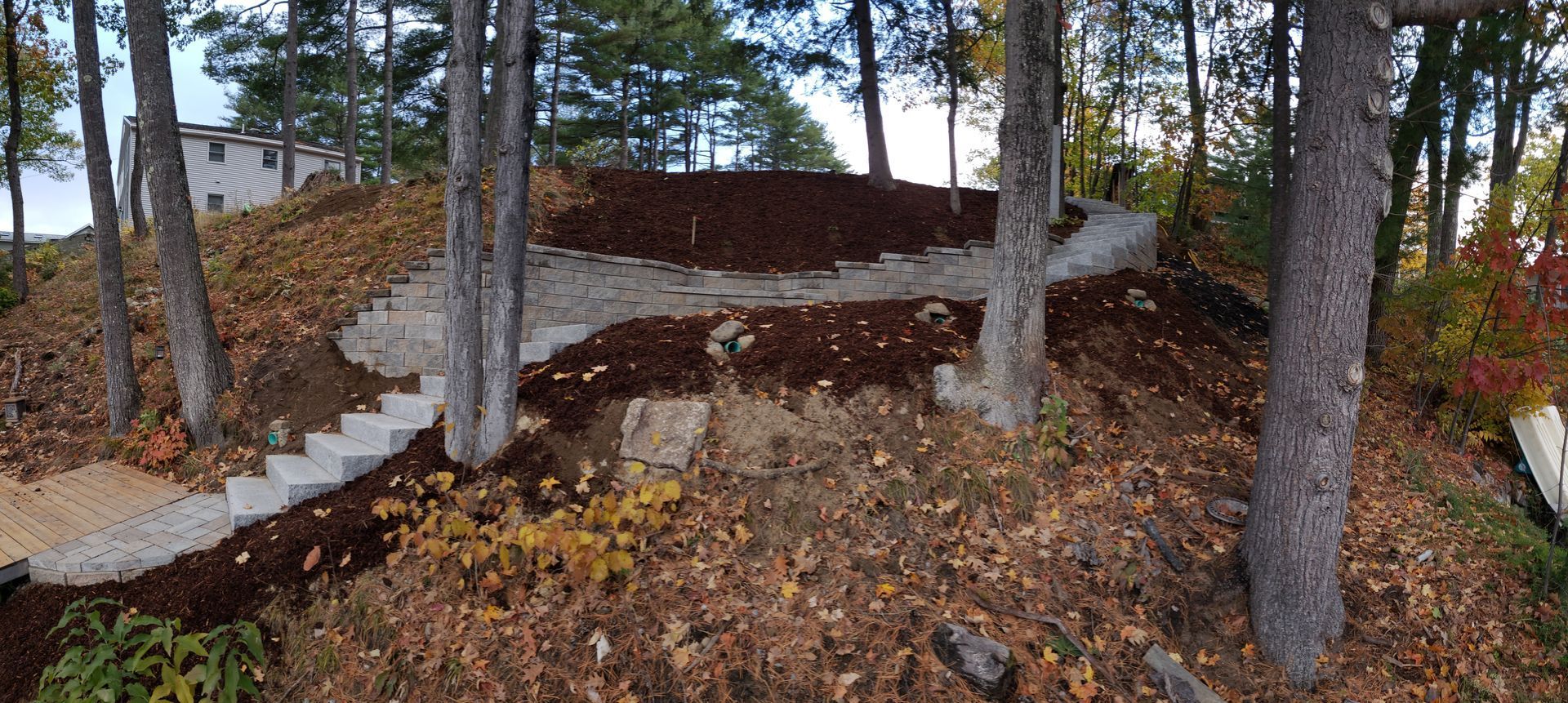 A set of concrete stone steps winds up a wooded hillside covered in brown mulch and fallen autumn leaves.