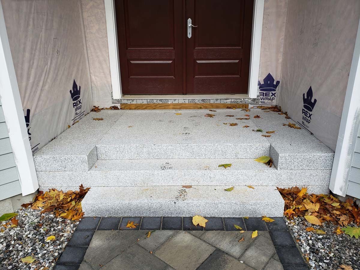 A set of three grey granite stairs leading to a double-door entrance with unfinished exterior walls.