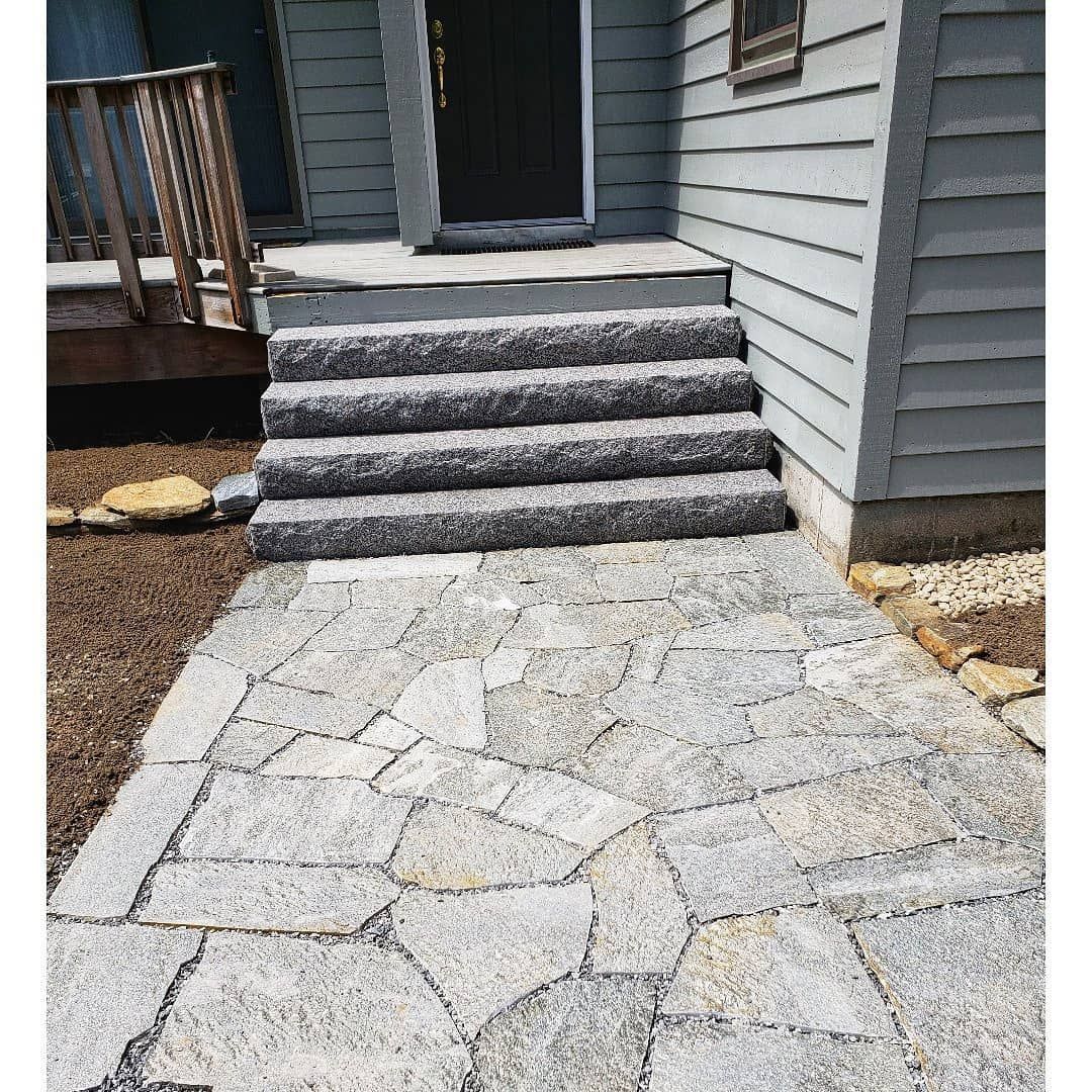 A stone walkway leads to four grey granite steps at the front entrance of a house with grey siding.
