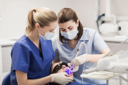 Two female dentists are working on a patient 's teeth in a dental office.