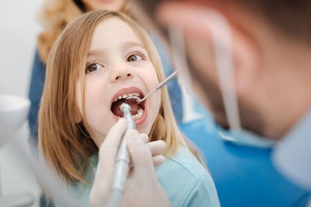 A little girl is getting her teeth examined by a dentist.