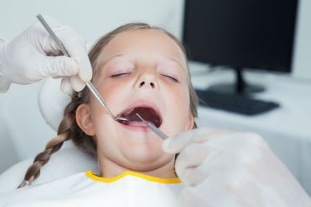 A little girl is getting her teeth examined by a dentist.