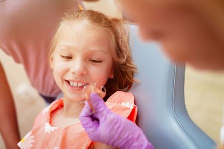 A little girl is sitting in a dental chair while a dentist examines her teeth.