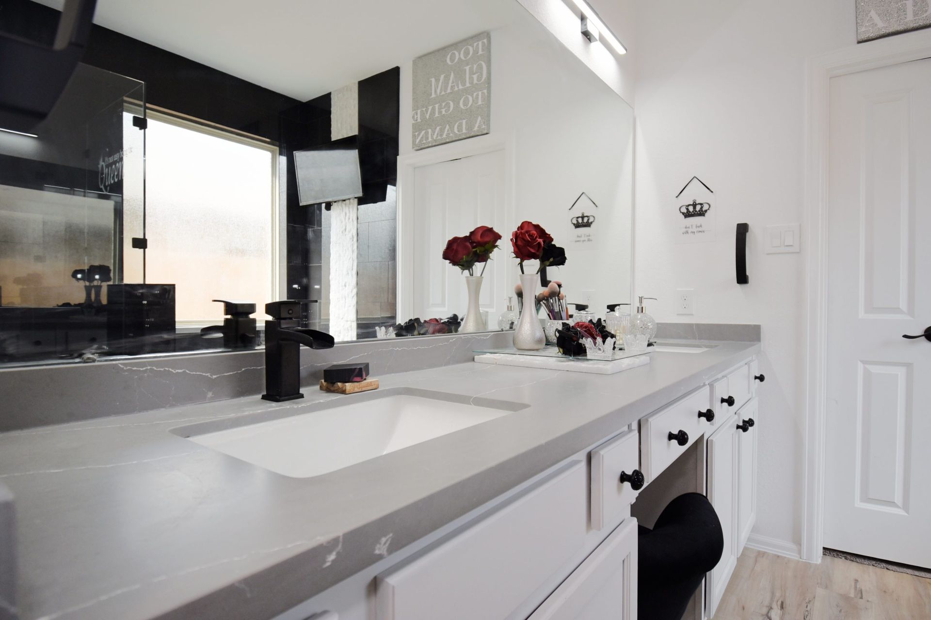 Bathroom with a long gray countertop, white cabinets, black fixtures, and a large mirror.