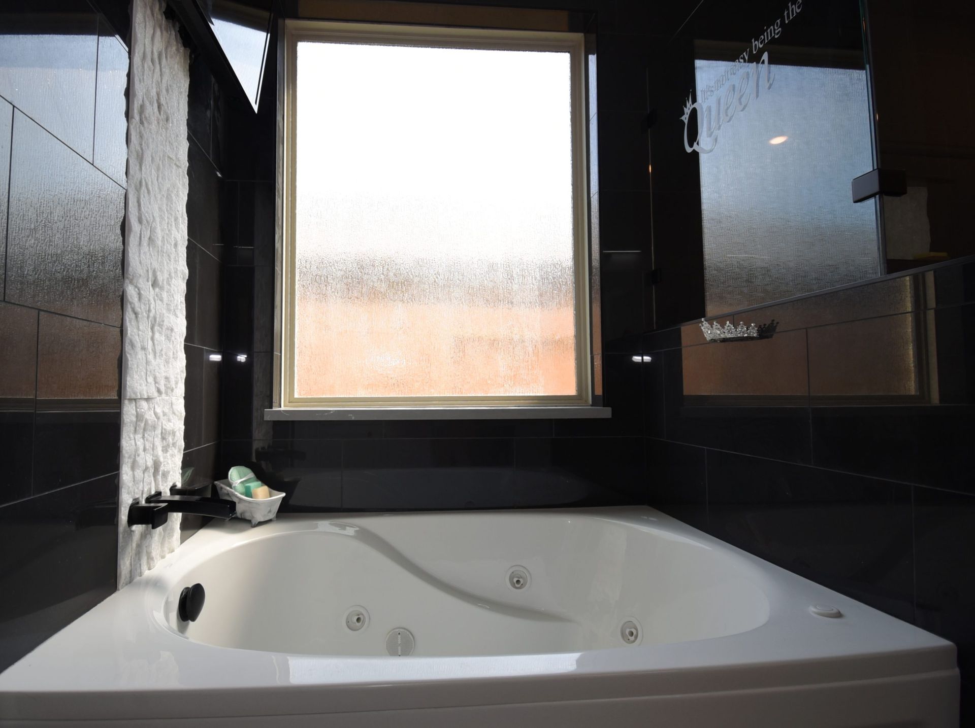 White jacuzzi tub in a black-tiled bathroom, with a window overlooking an orange building.