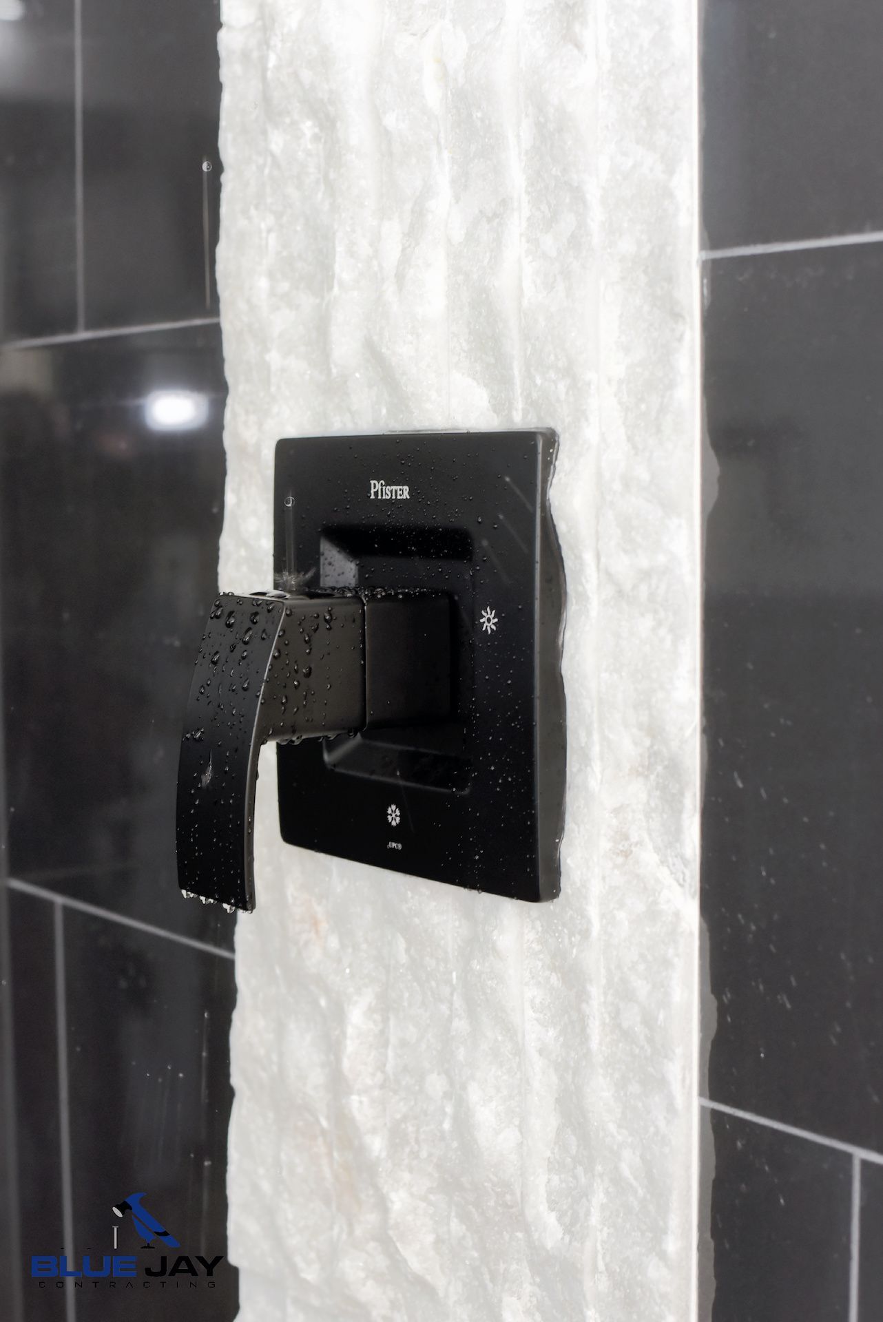 Black shower faucet with textured white stone accent on a black tiled wall.