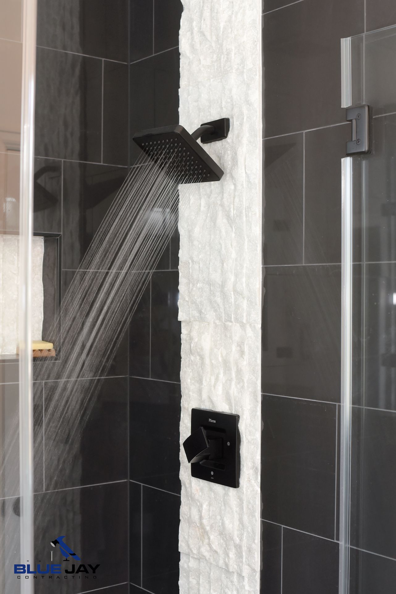 Shower with black fixtures and dark gray tile, featuring a white stone accent strip.