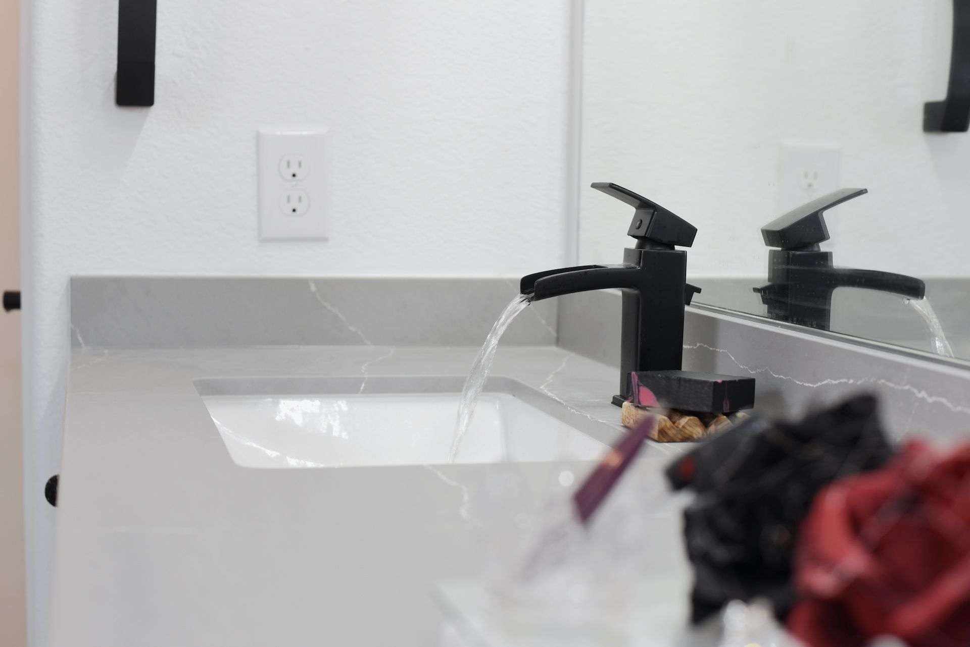 Black faucet with water flowing into a white sink, on a gray countertop, in a bathroom.