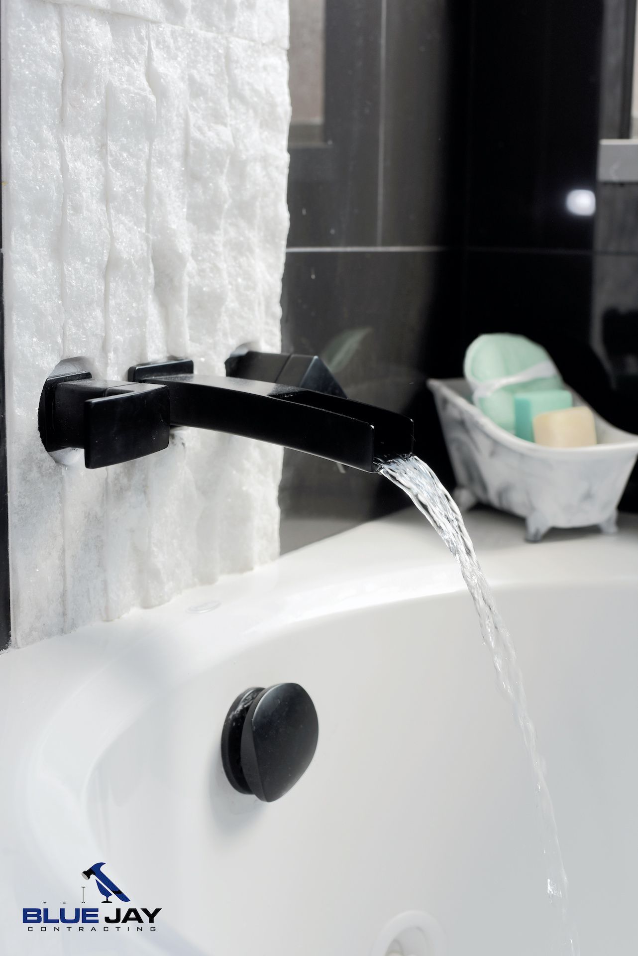 Black bathtub faucet with running water, white tub, and textured white wall tile.