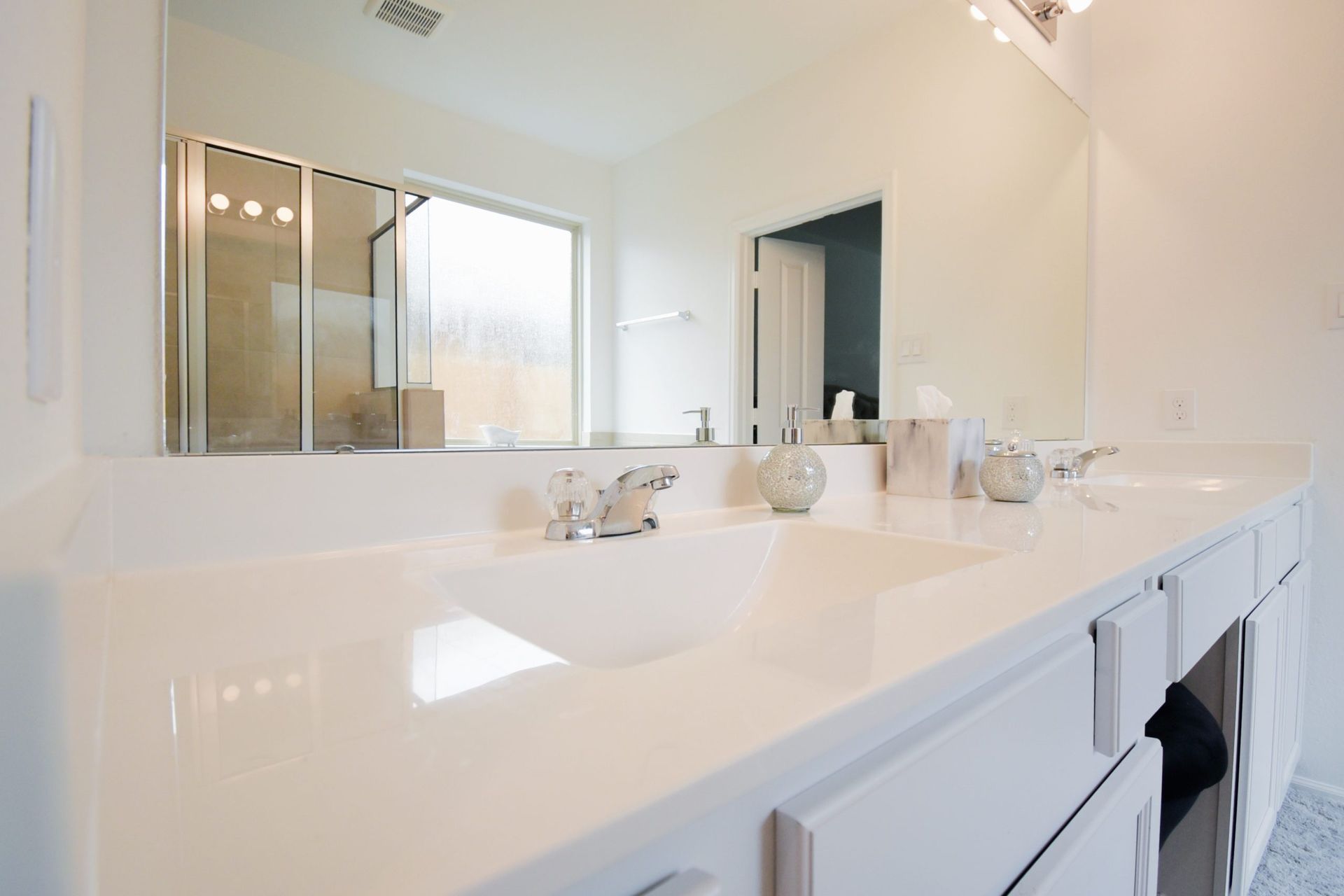 White bathroom with double sinks, large mirror, and glass shower.