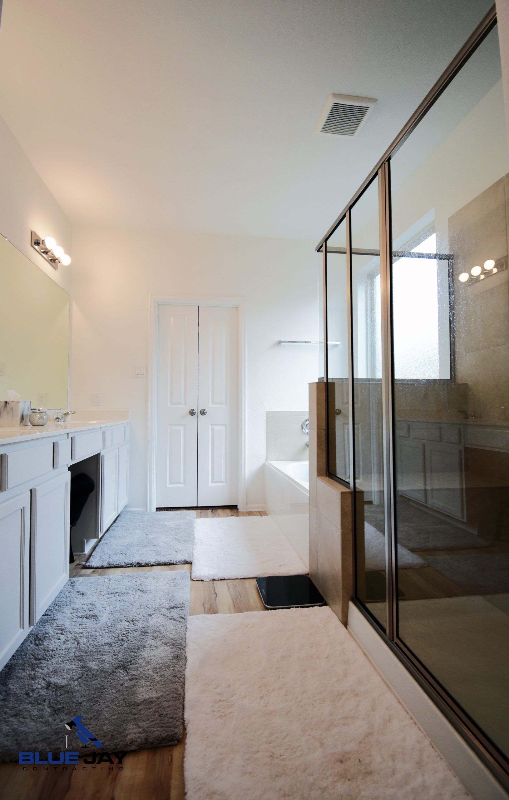 Spacious white bathroom with glass shower, white cabinets, and a large mirror.