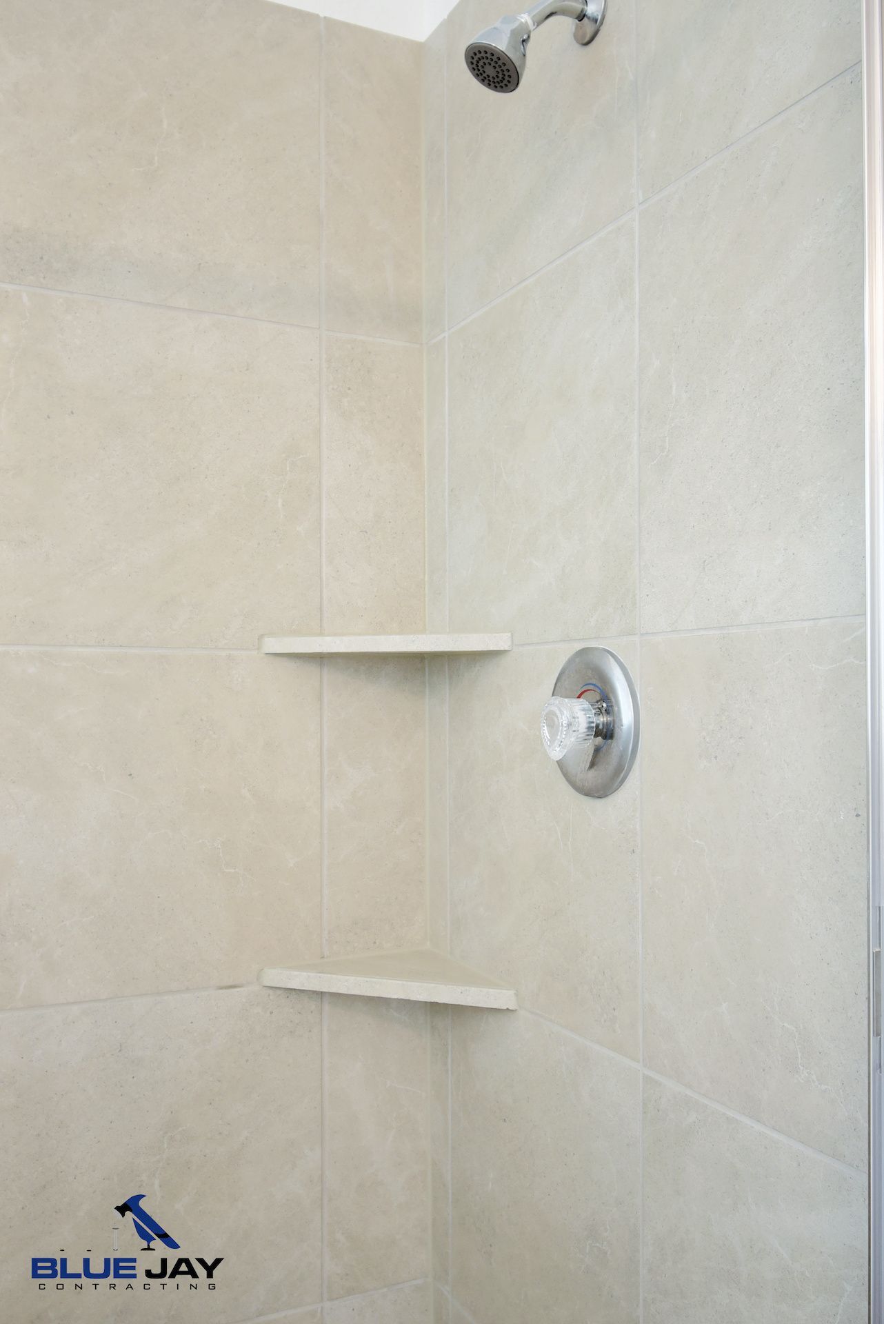 Shower with light-beige tiled walls, two built-in shelves, a showerhead, and chrome fixtures.