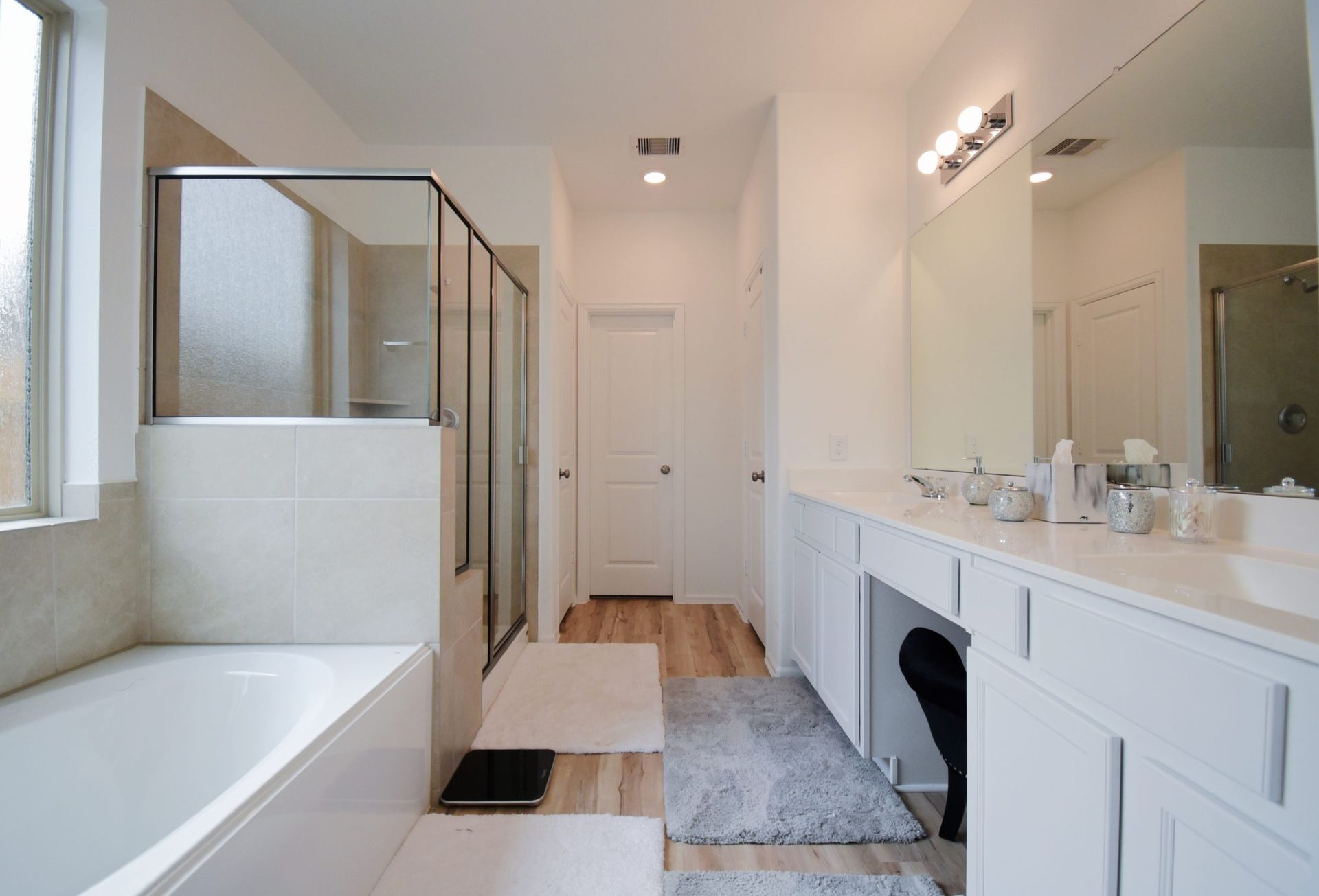 Bright bathroom with a bathtub, shower, double sink vanity, and hardwood floor.