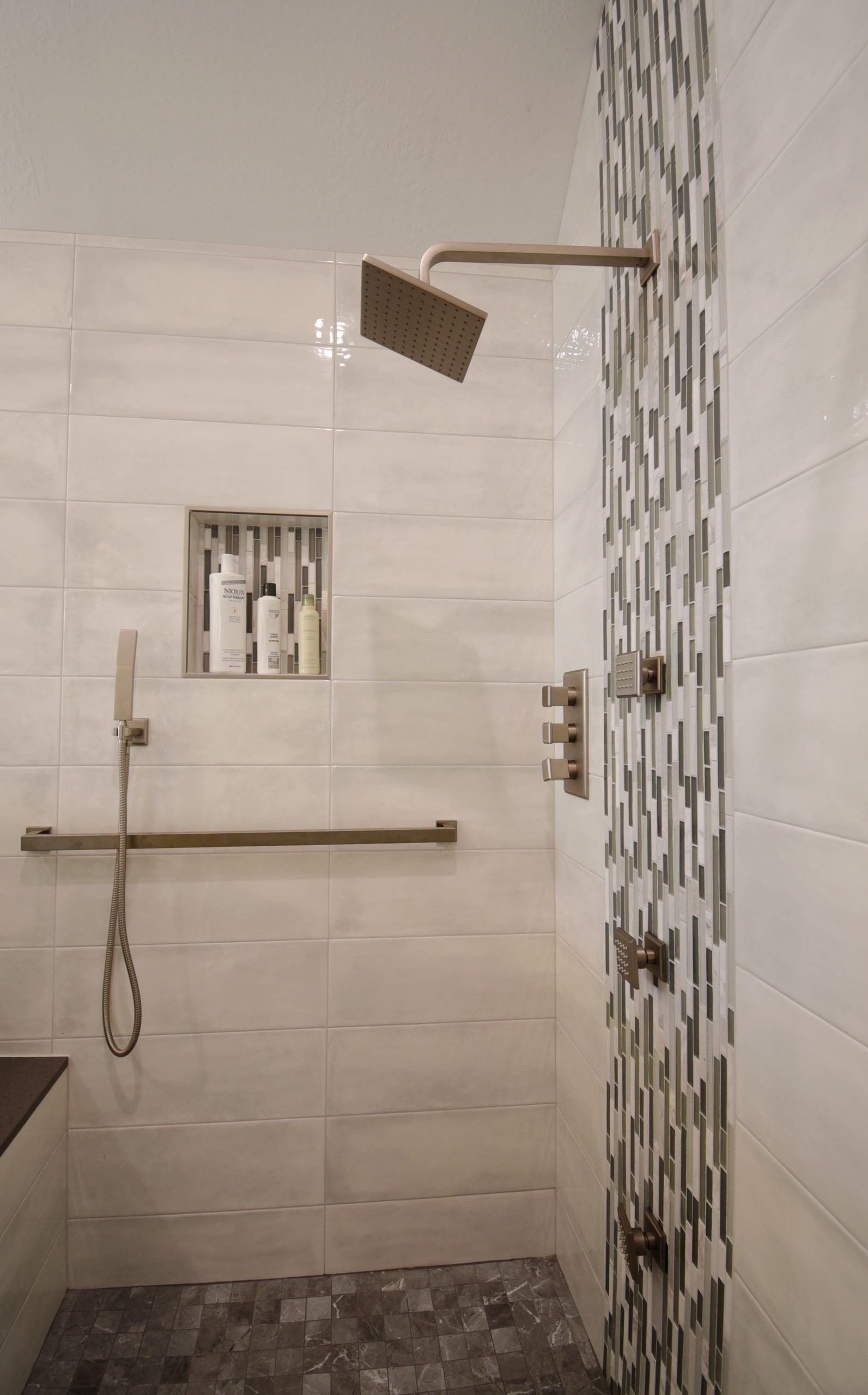 Accessible shower with grab bar and mosaic tile accents; neutral tones, a bench.
