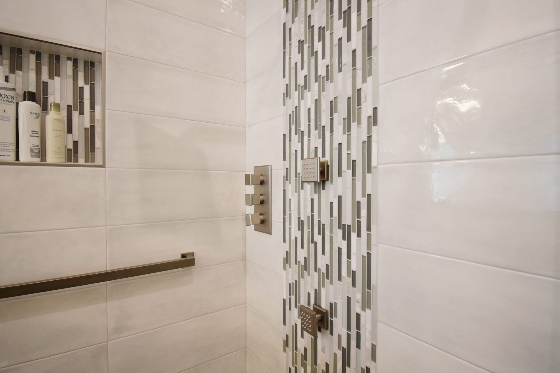 Shower interior with white tile walls, a decorative vertical strip, and a grab bar.