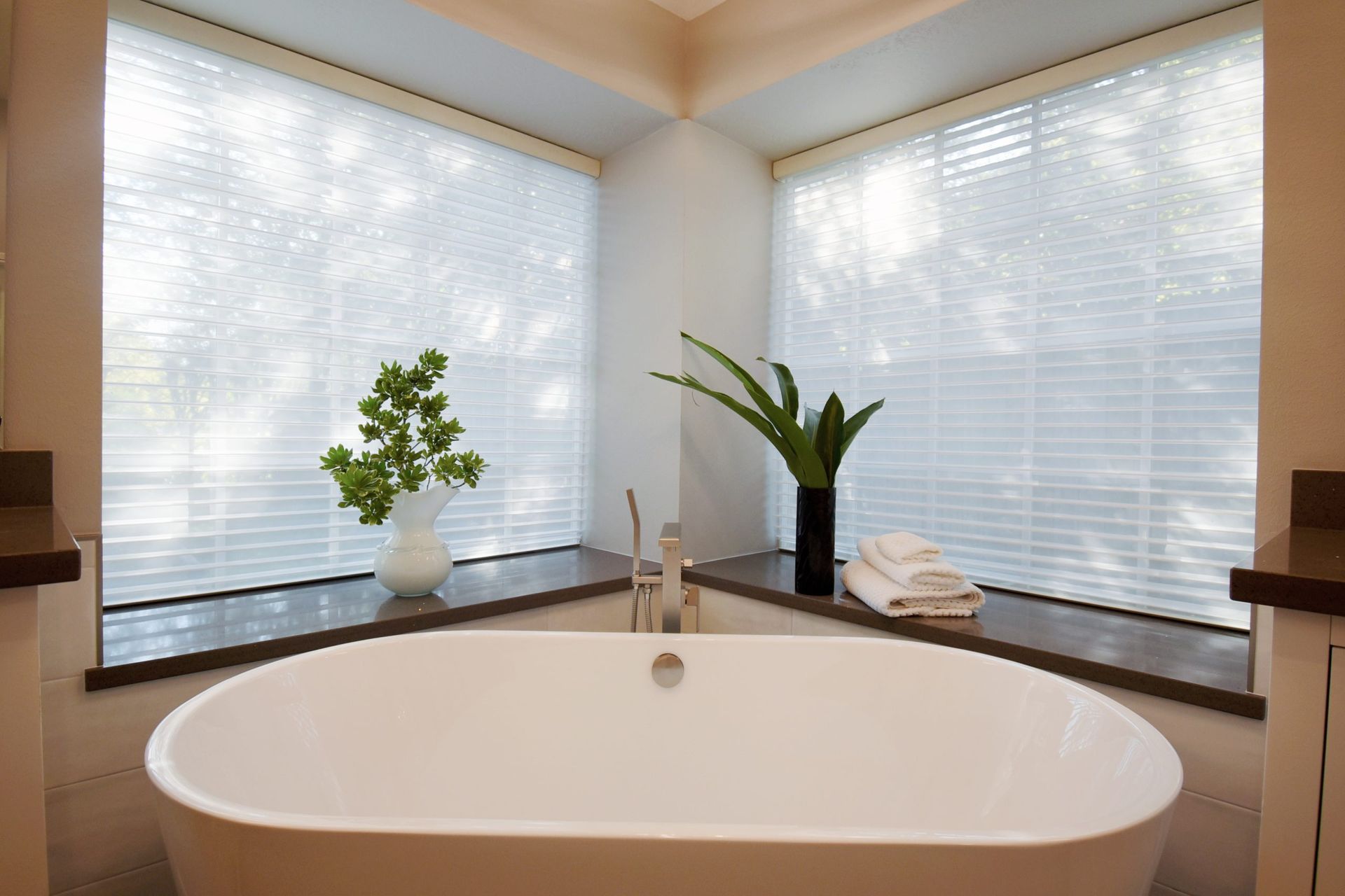 Bathroom with oval tub, corner windows, and green plants.