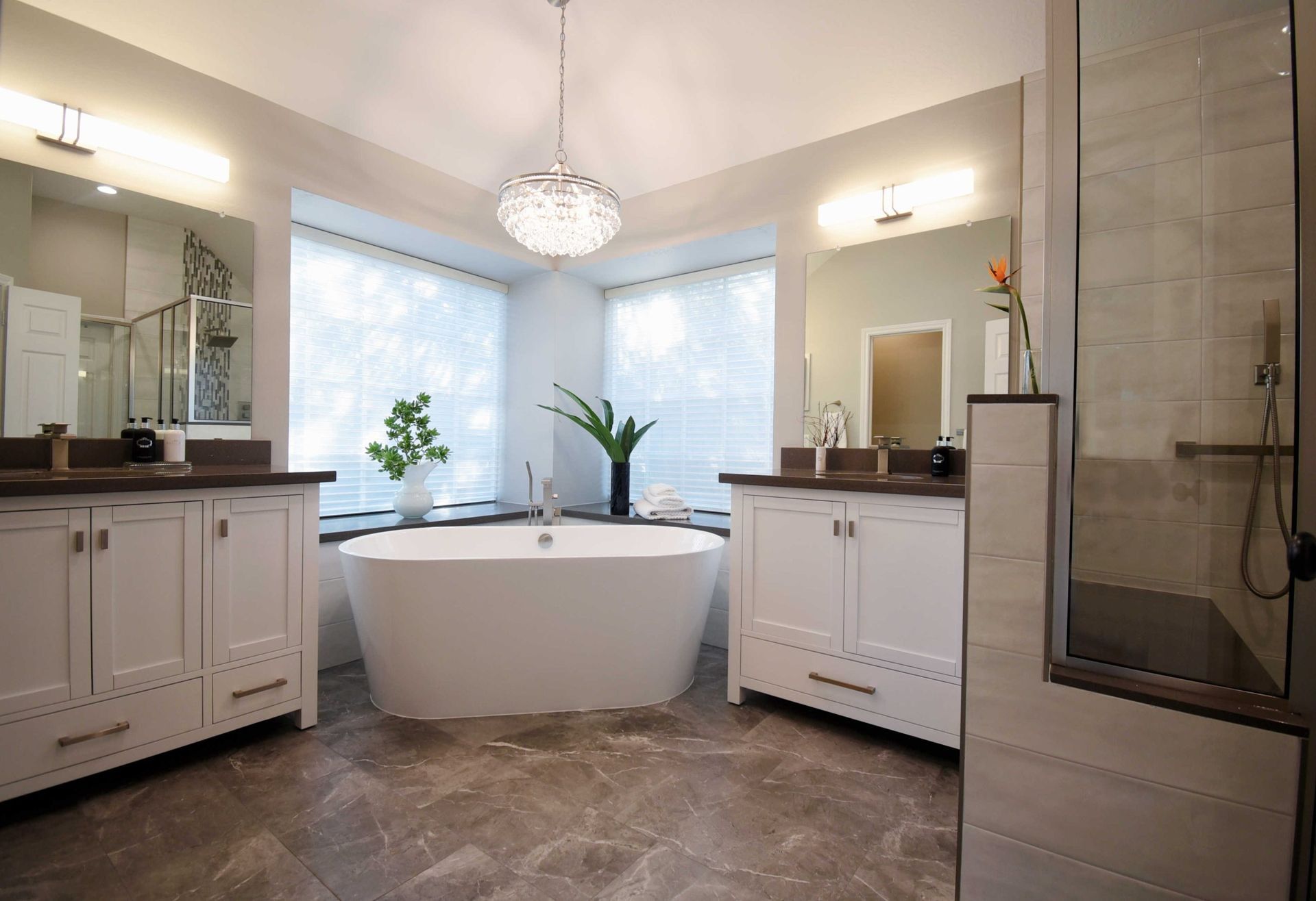 Luxurious bathroom with white cabinets, a freestanding tub, and a crystal chandelier.
