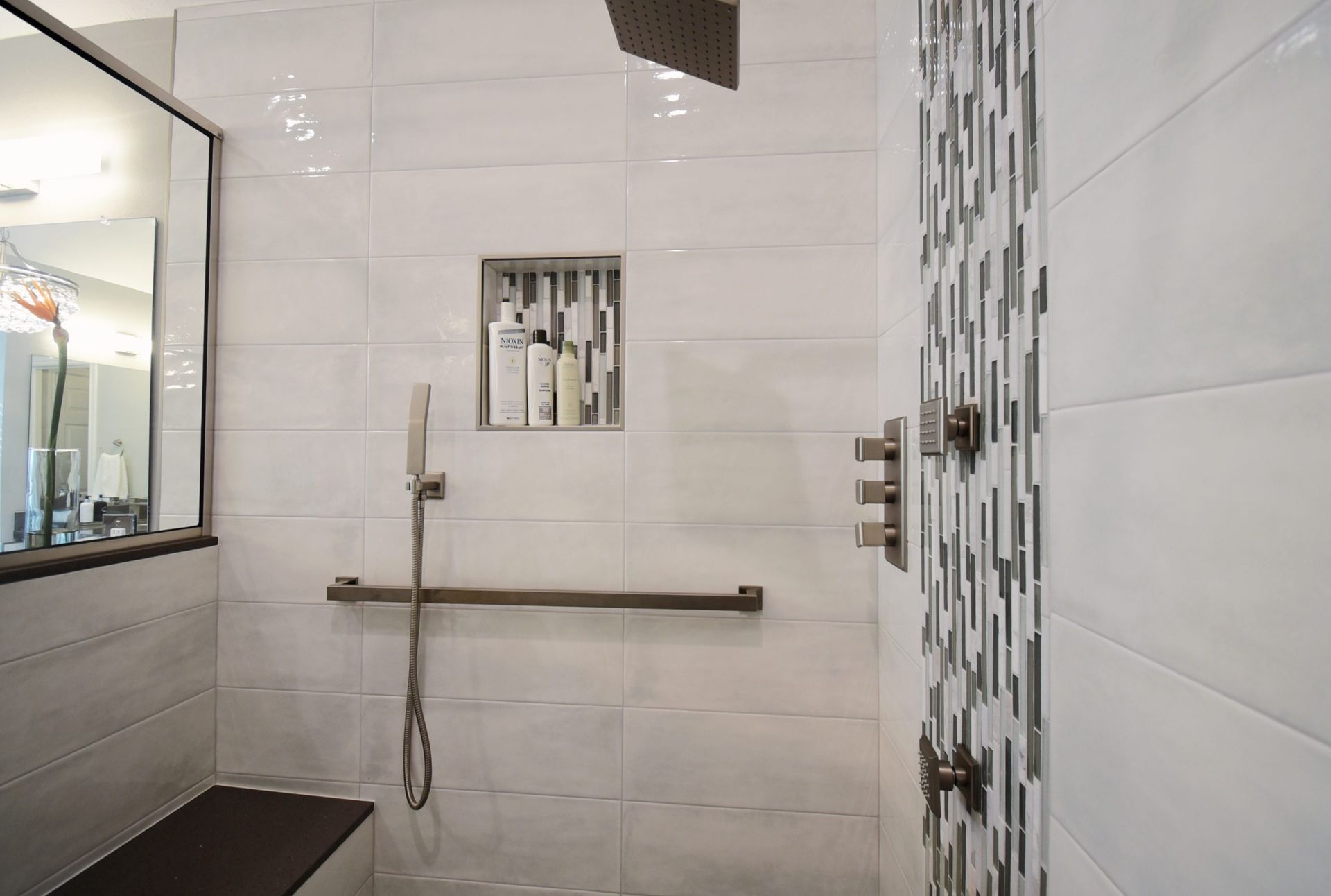 White tiled shower with built-in bench and shampoo niche.  Handheld showerhead, grab bar, and mosaic accent.