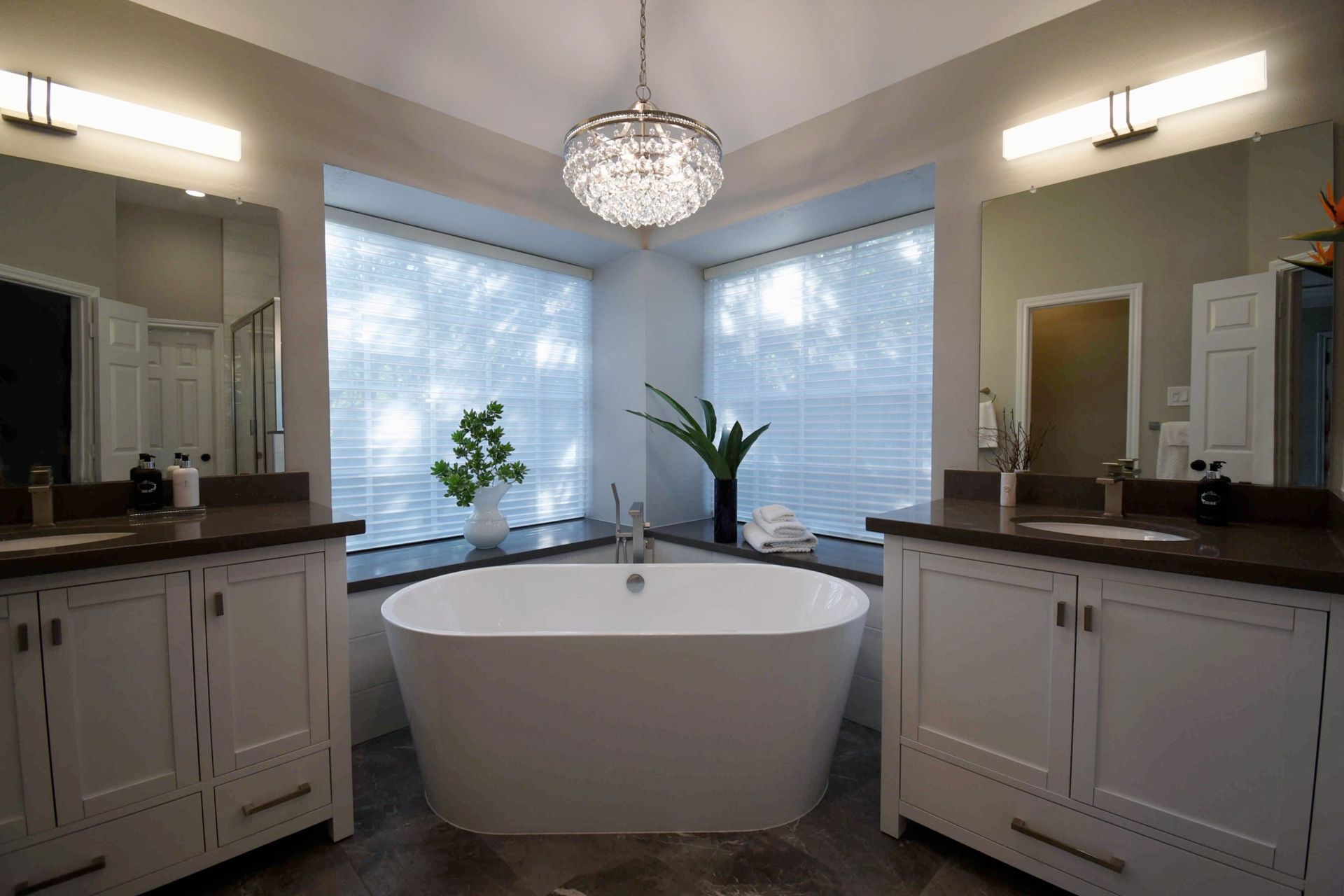 Modern bathroom with white soaking tub, dual vanities, and crystal chandelier.