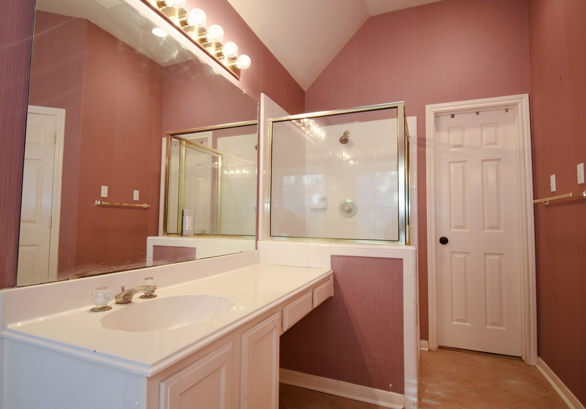 Bathroom with a white sink and cabinet, shower, door, and pink walls.