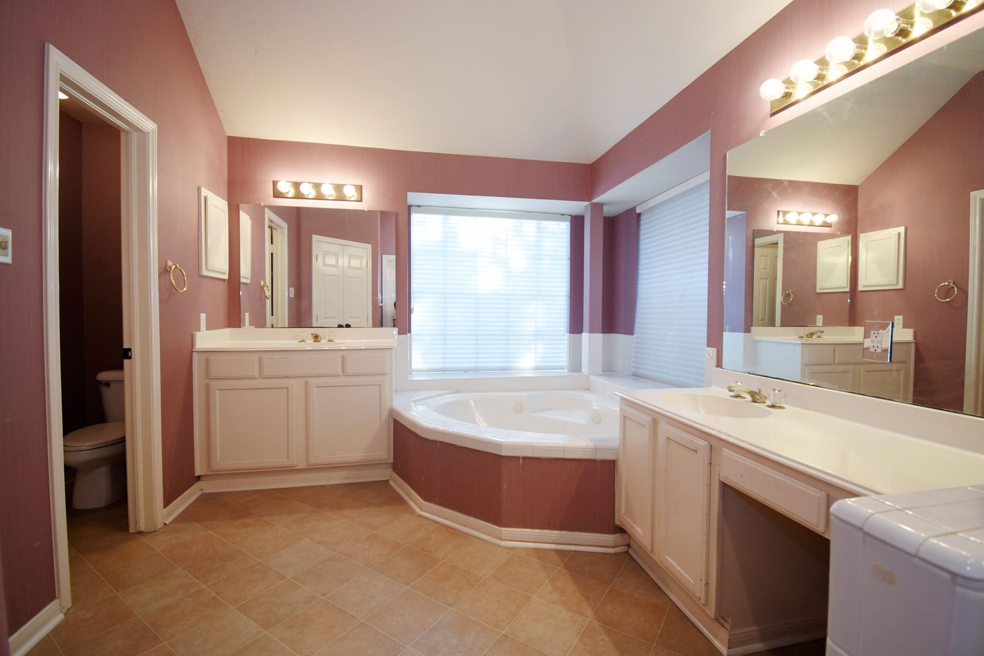 Pink-walled bathroom with a white bathtub and vanity, two sinks, and a toilet visible.