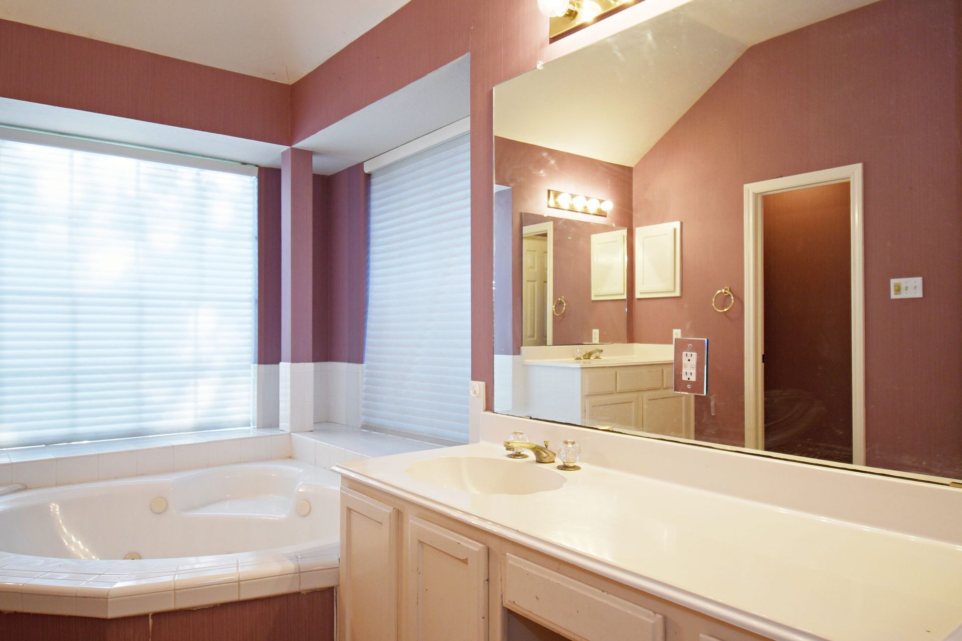 Bathroom with bathtub, vanity, and large mirror; pink walls and white cabinets.