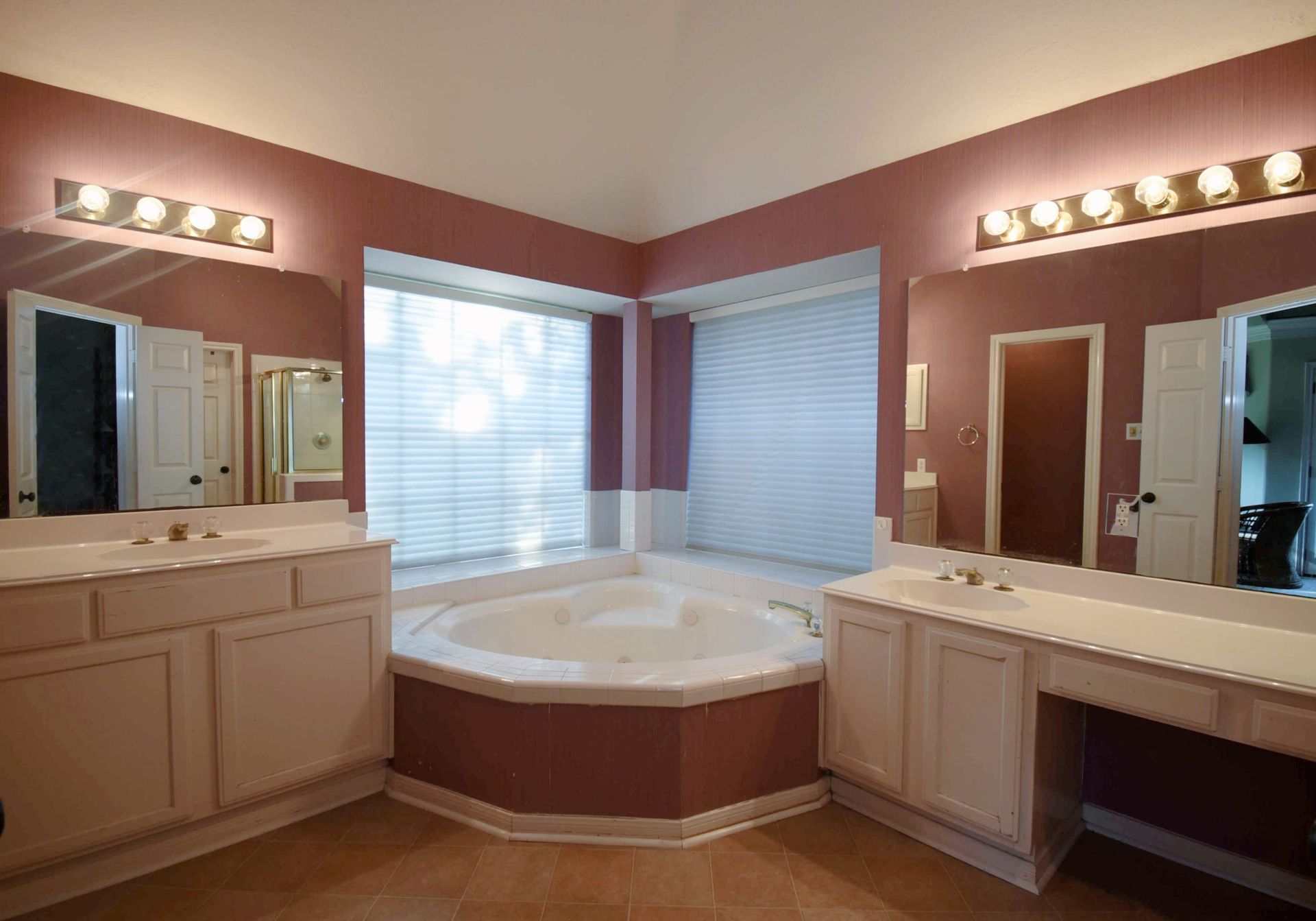 Spacious bathroom with pink walls, a corner jacuzzi tub, and dual vanities with mirrors.