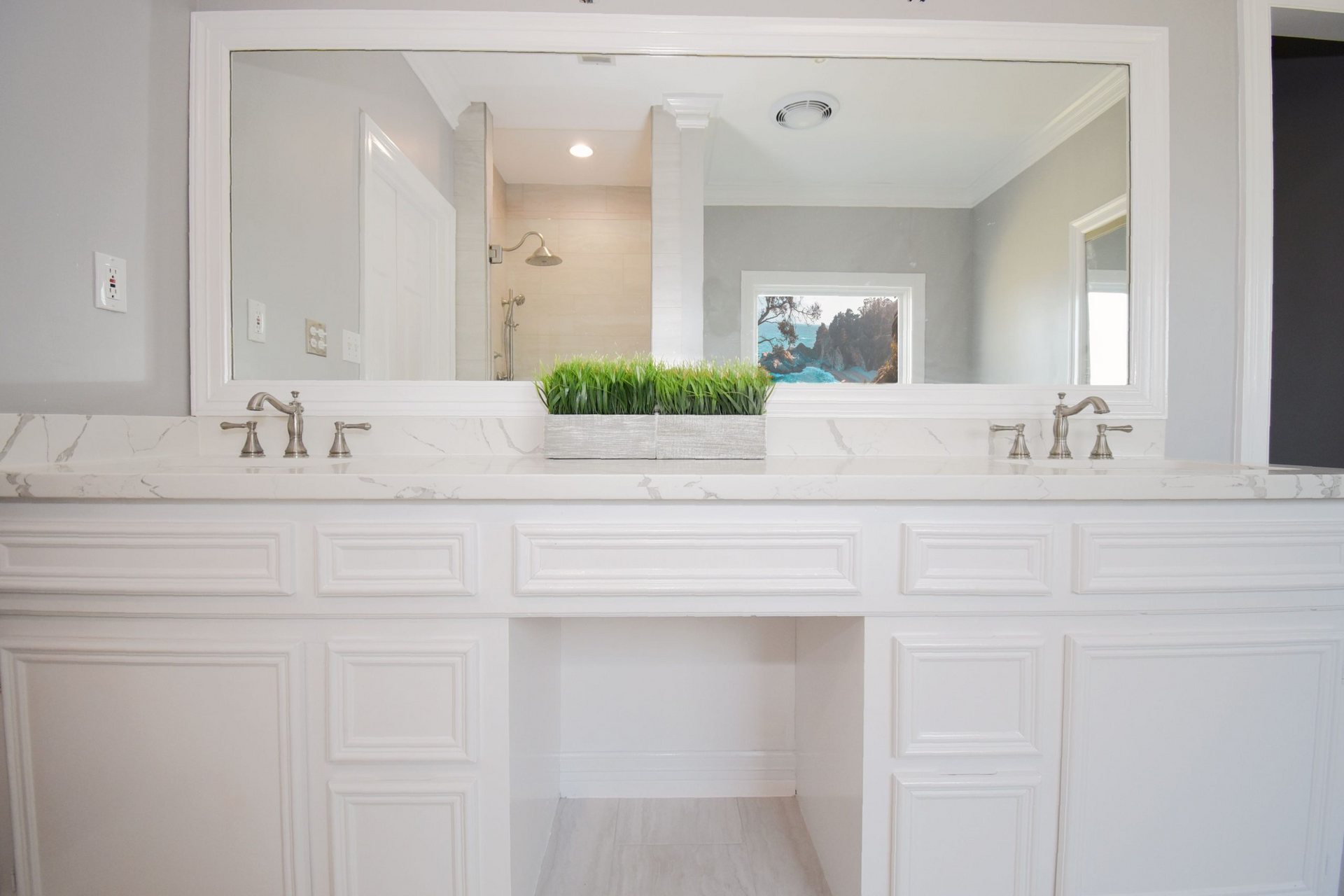 White double vanity with marble countertop, large mirror, and a green plant in a bathroom.