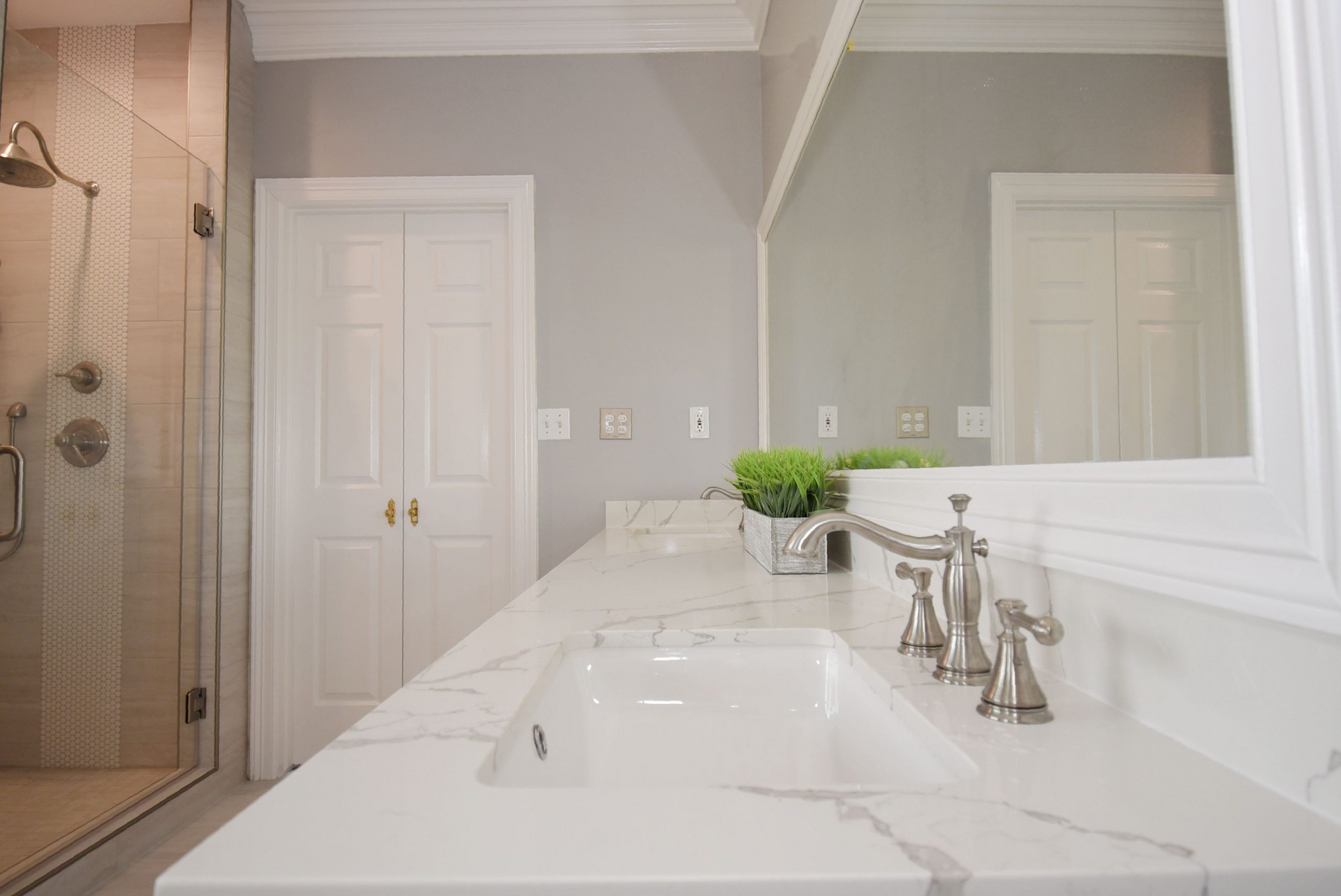 Bathroom with white countertop, marble-like finish, silver fixtures, and a large mirror.