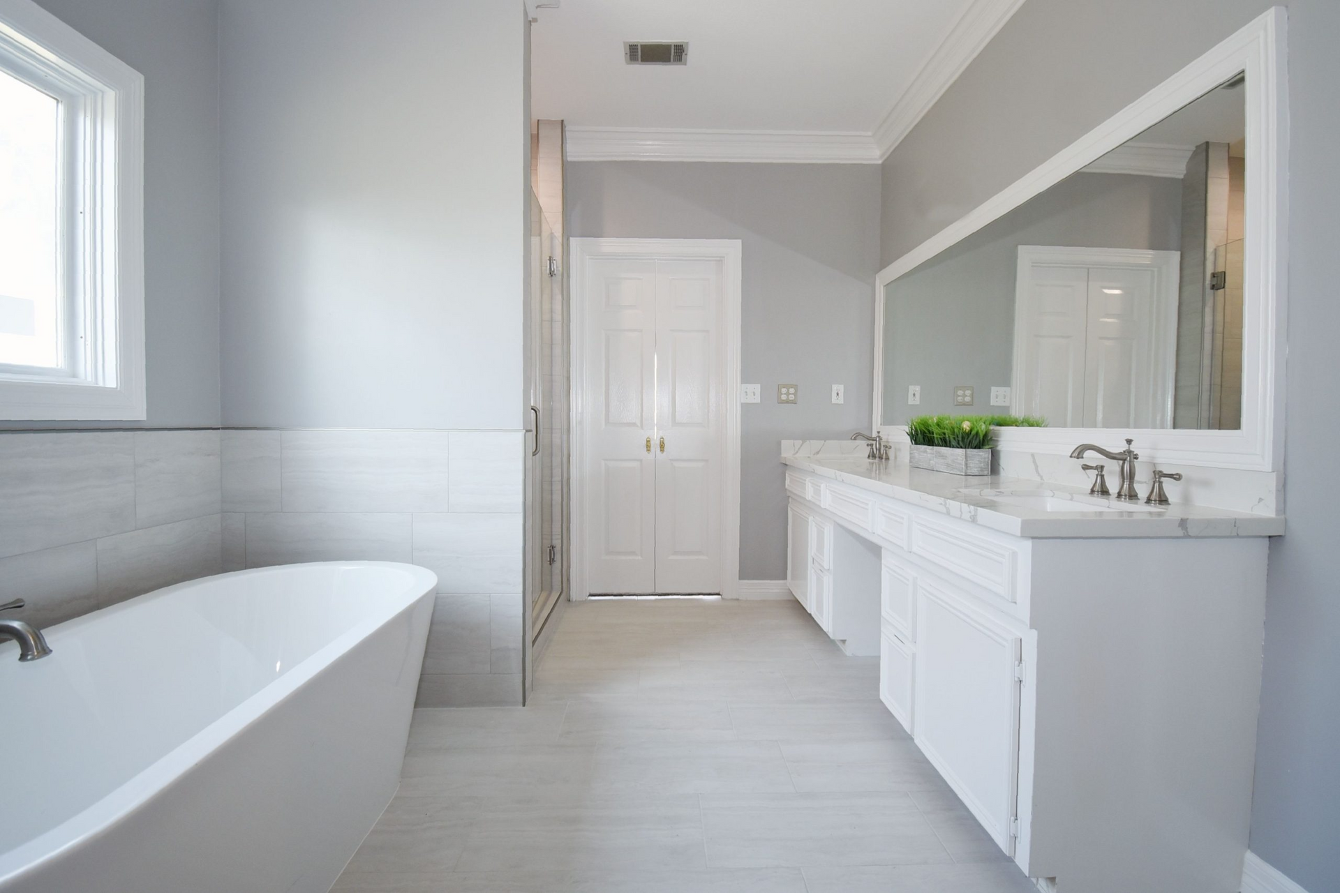 Spacious, modern bathroom with a white freestanding tub, white vanity, and gray walls.
