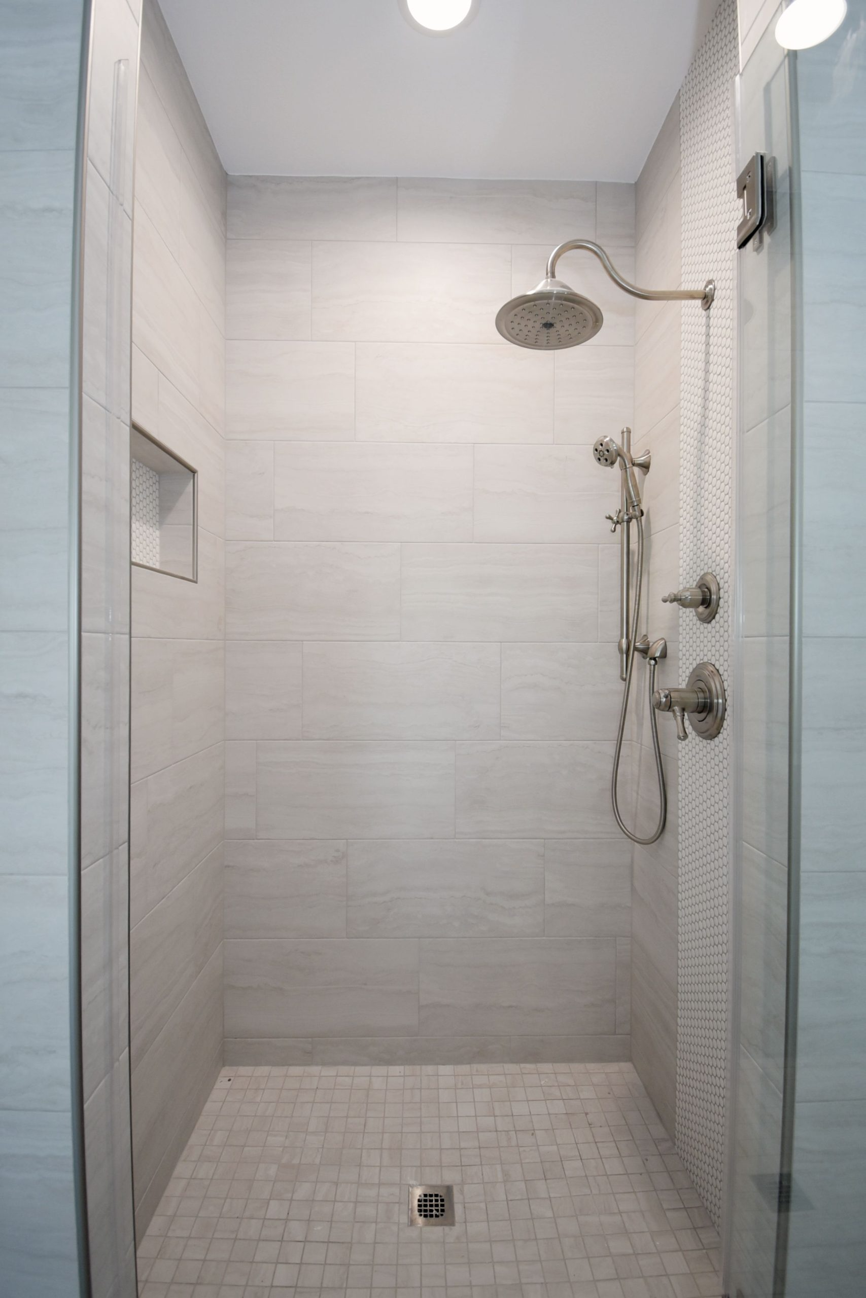 Small modern shower with gray tiles and glass door, stainless steel fixtures, and a rain showerhead.