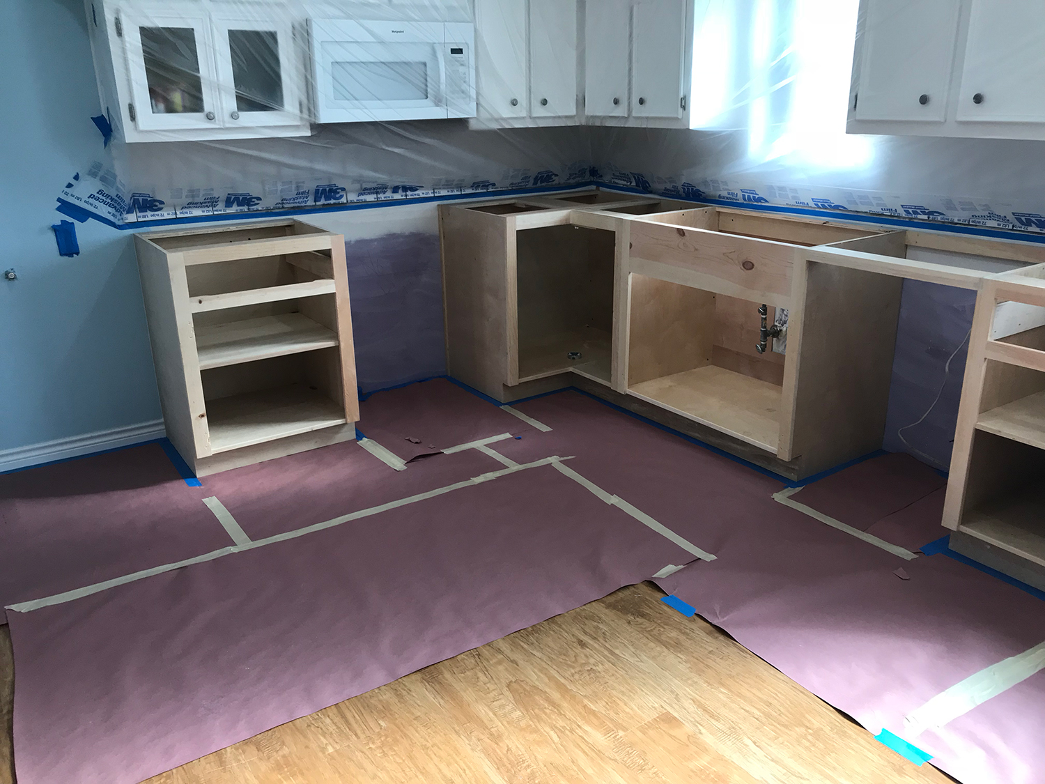 Kitchen cabinets being installed, walls and floor covered for protection.