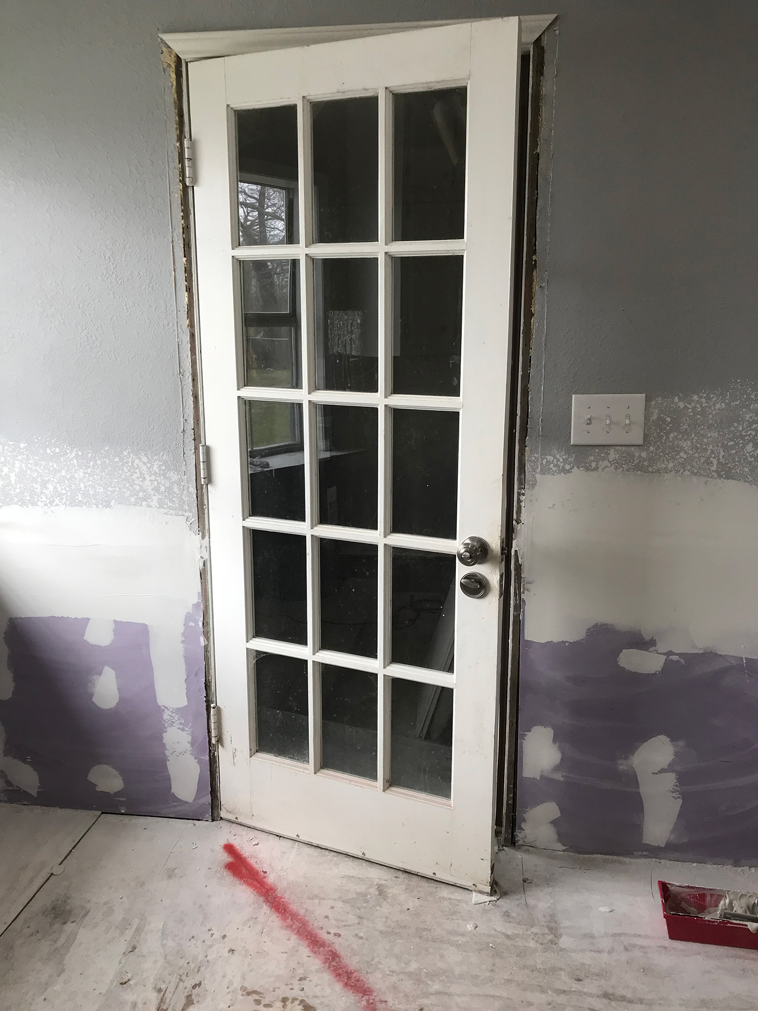 White-paneled door slightly ajar in a room under renovation; walls are gray and white.