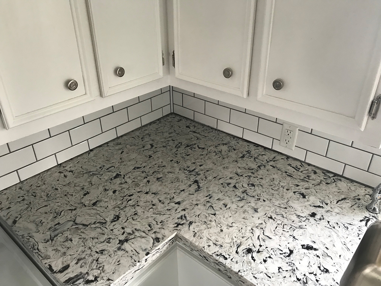 Kitchen corner with white cabinets, subway tile backsplash, and gray quartz countertop.