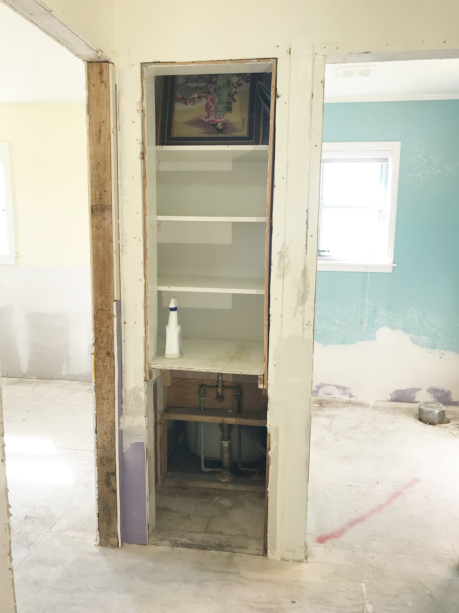 Built-in shelving unit in a wall during renovation. Shelves are white, walls are exposed, and space is dusty.
