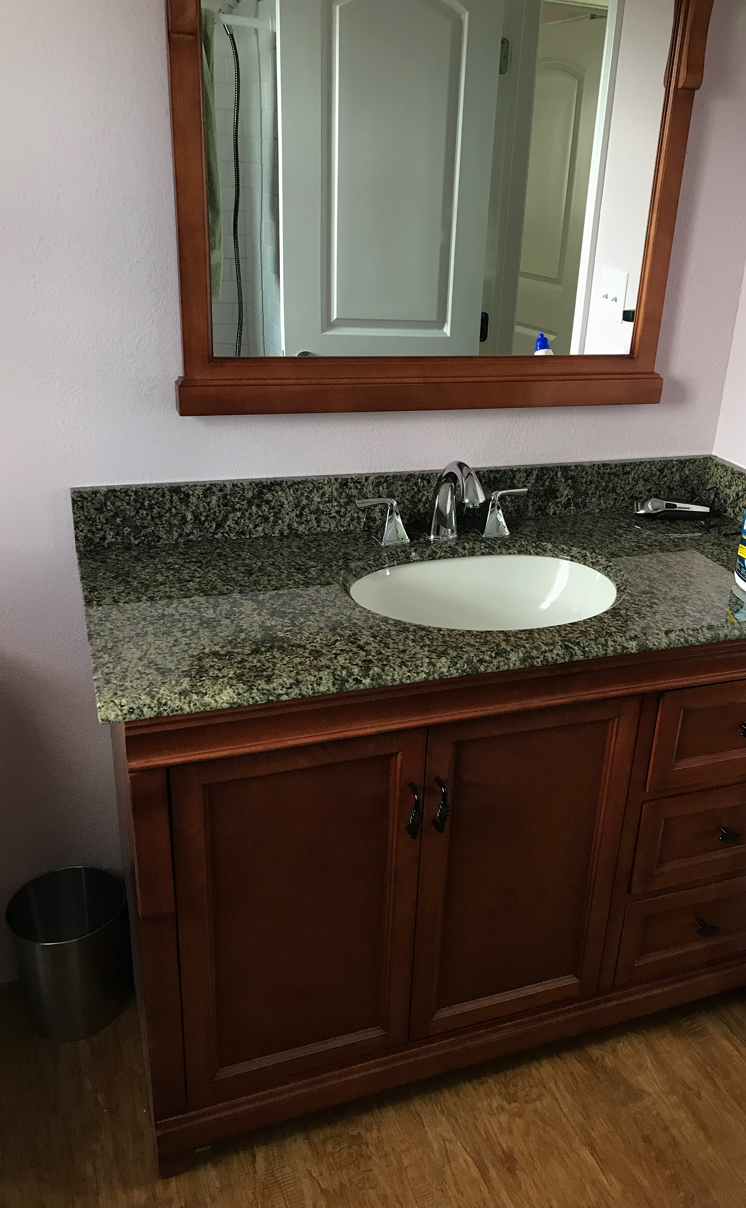 Bathroom vanity with brown cabinets, granite countertop, oval sink, and mirror.