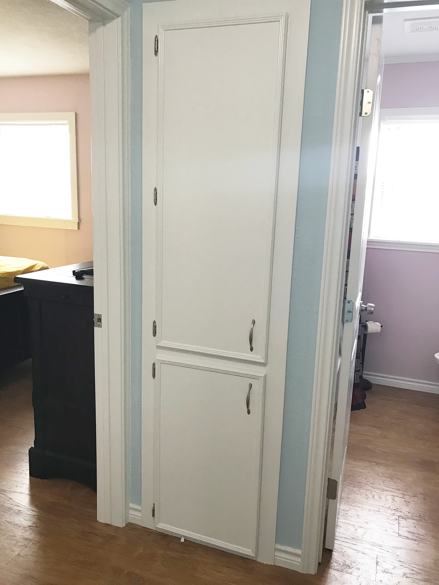 A white closet in a hallway between a pink bedroom and a light-blue-walled bathroom.