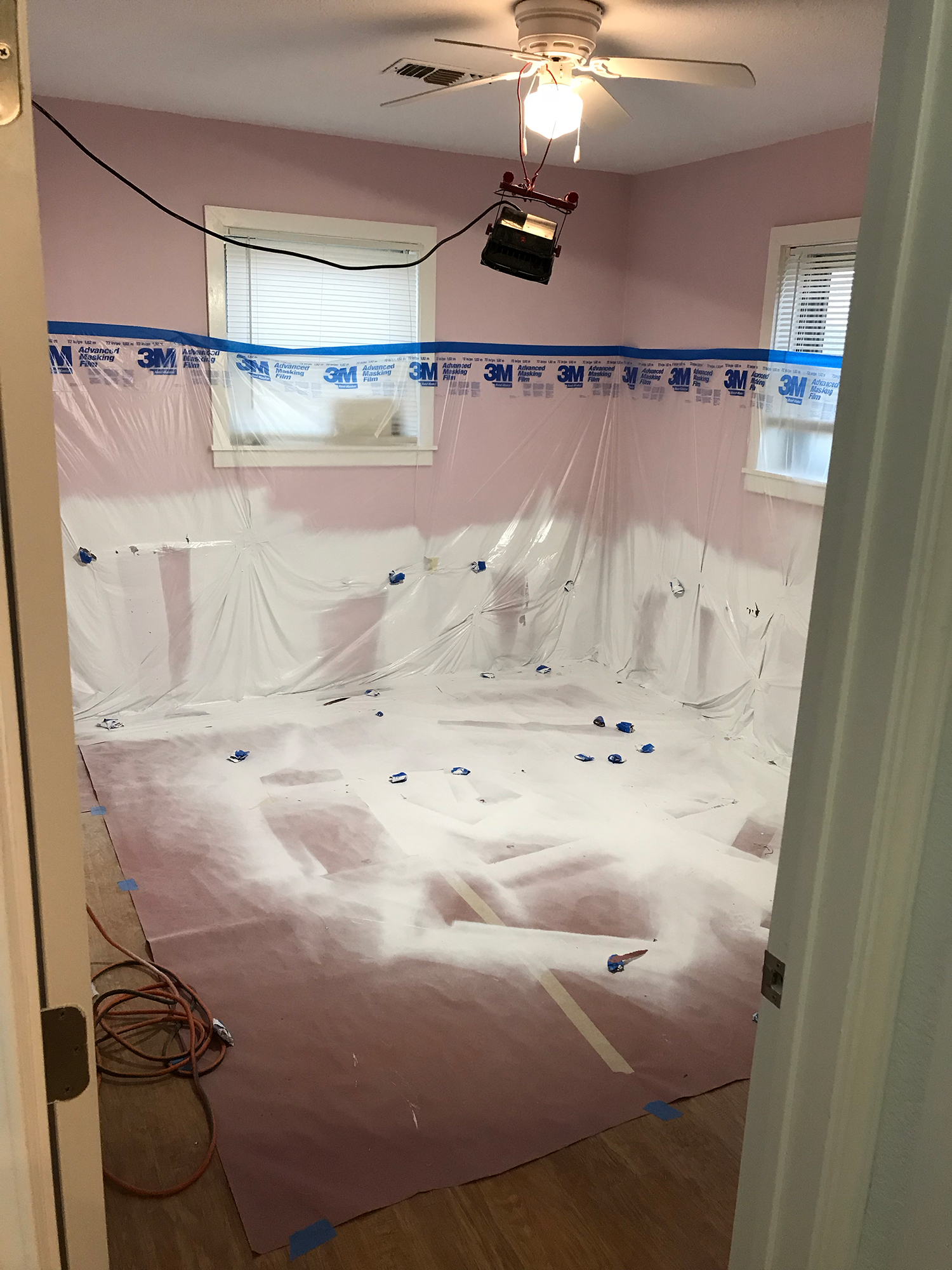 A room prepared for painting, with plastic sheeting covering walls, windows, and floor; pink walls.