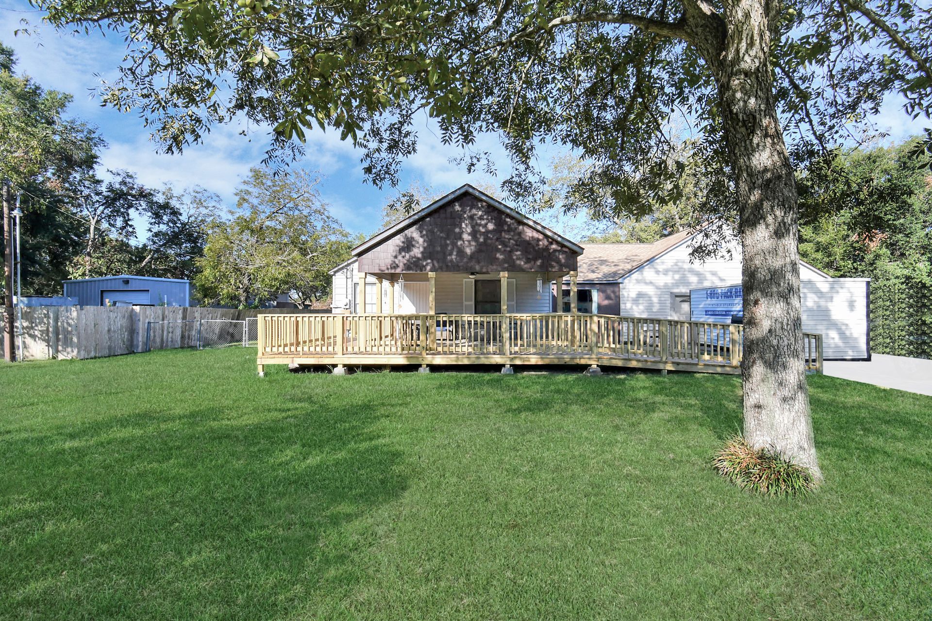 House with wooden deck and green lawn under a tree.