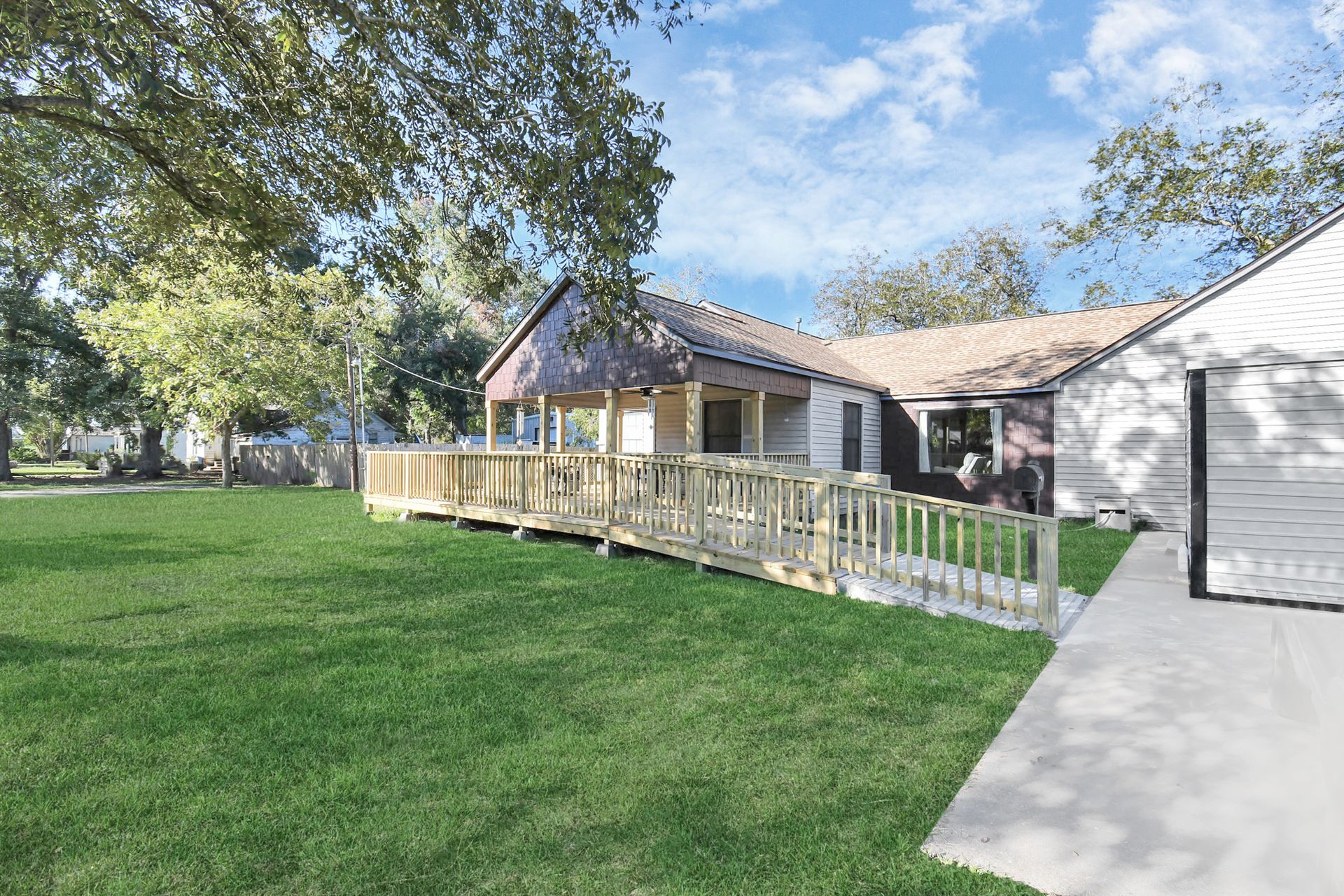 A house with a wooden ramp for accessibility, green lawn, and trees under a blue sky.