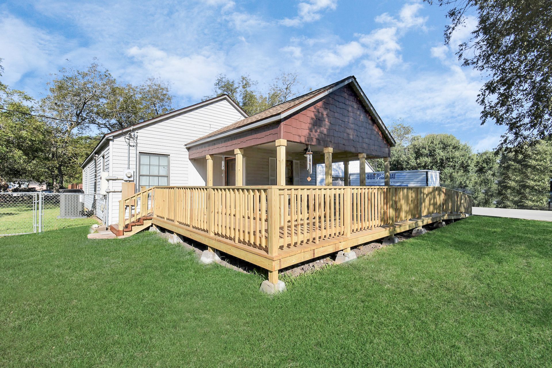 House with wooden deck and porch; green lawn and blue sky.
